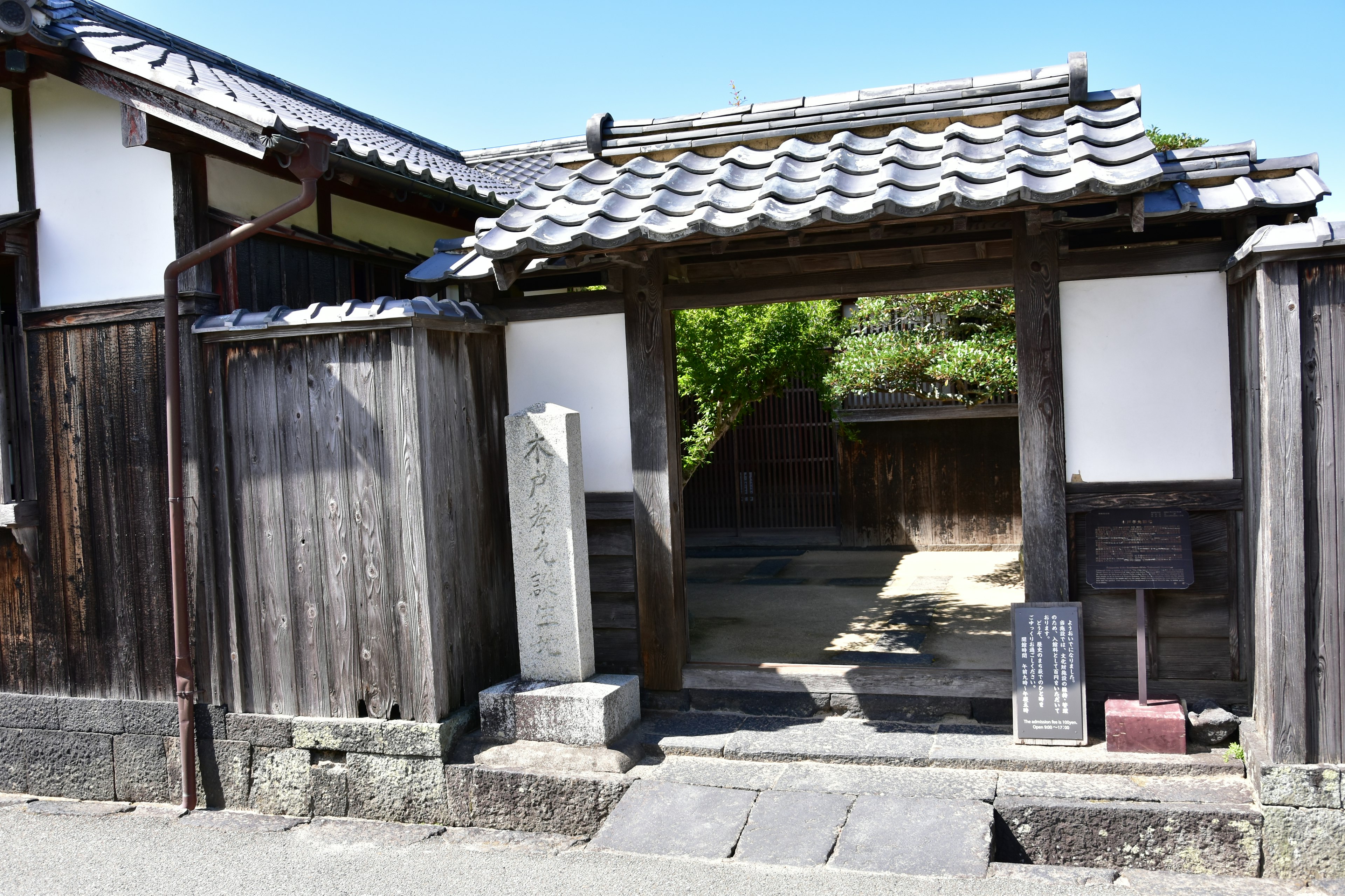 Traditional Japanese building entrance with wooden gate and tiled roof, stone plaque visible