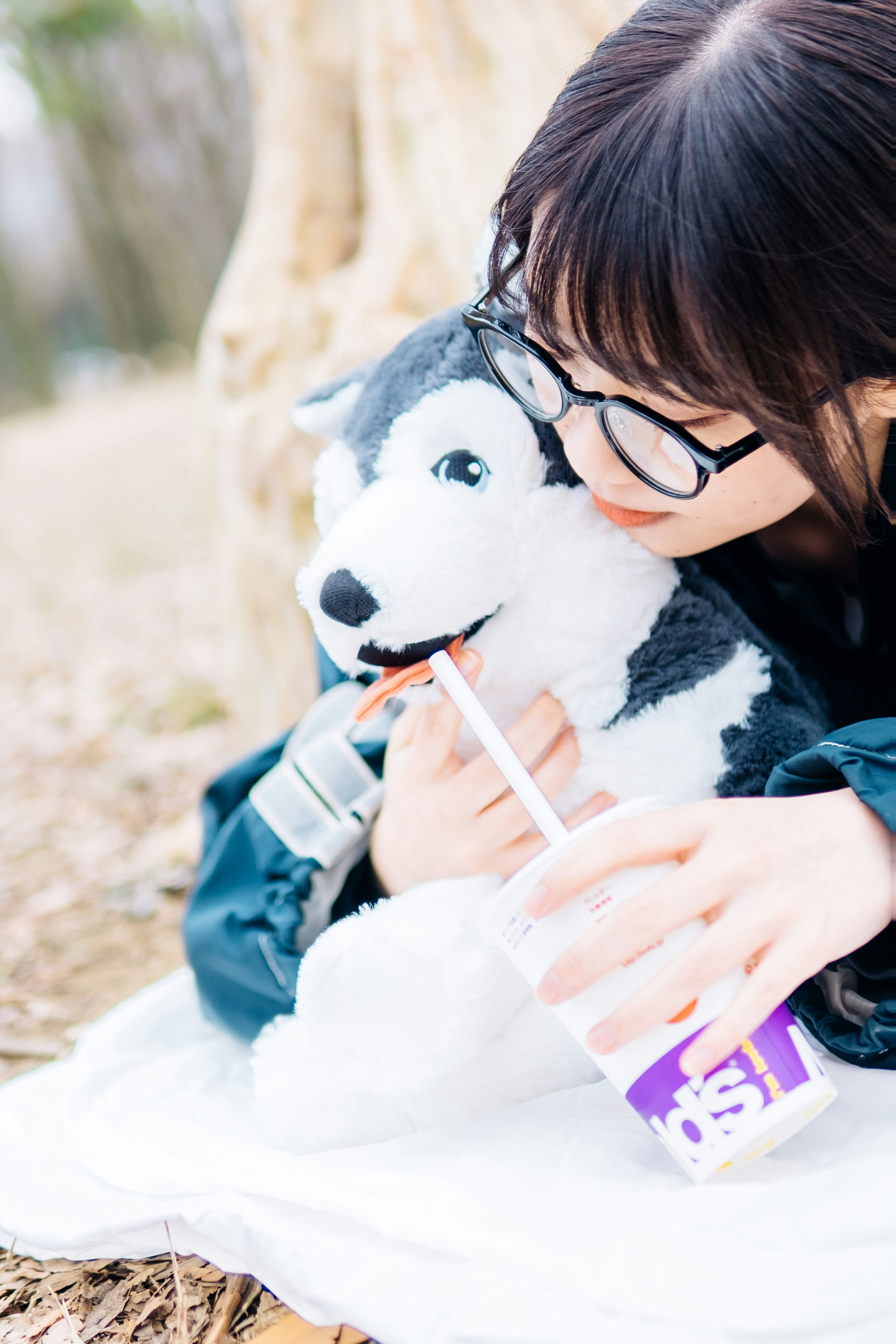 A woman cuddling a stuffed husky while holding a drink