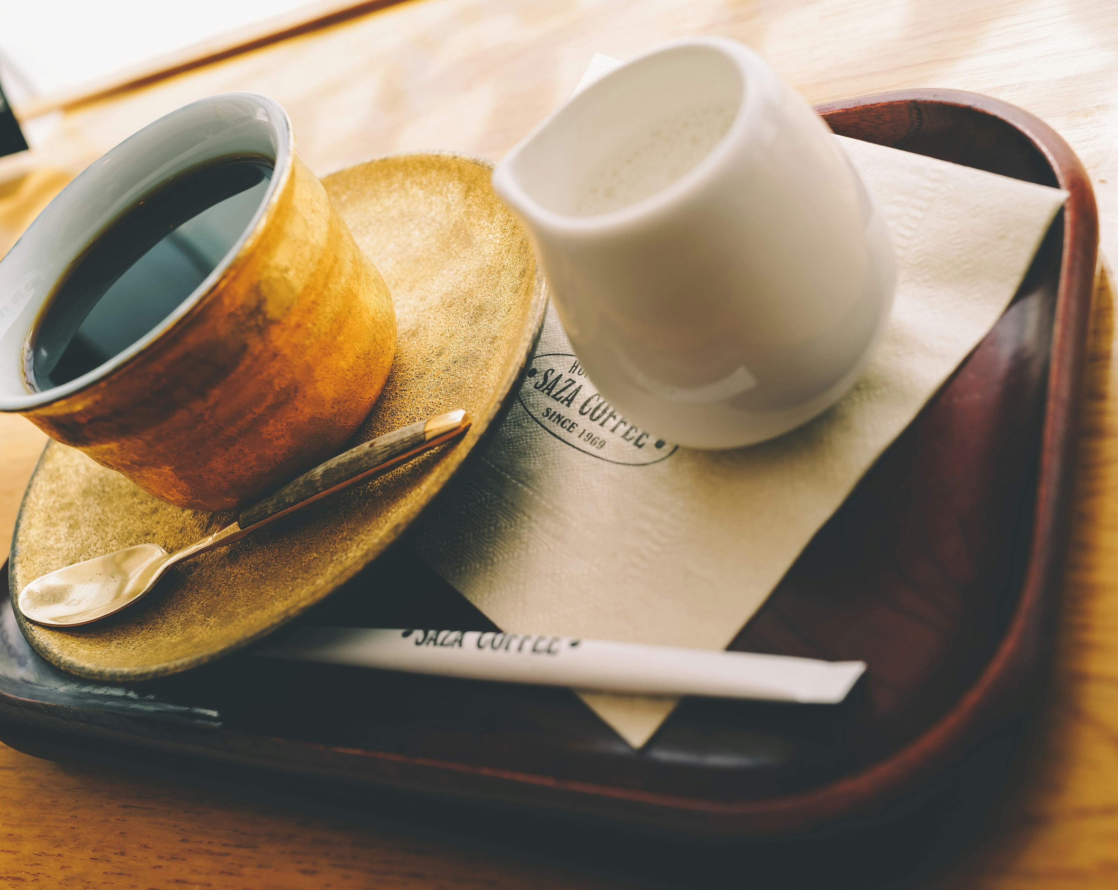 A golden coffee cup with a spoon on a tray with cream and a napkin