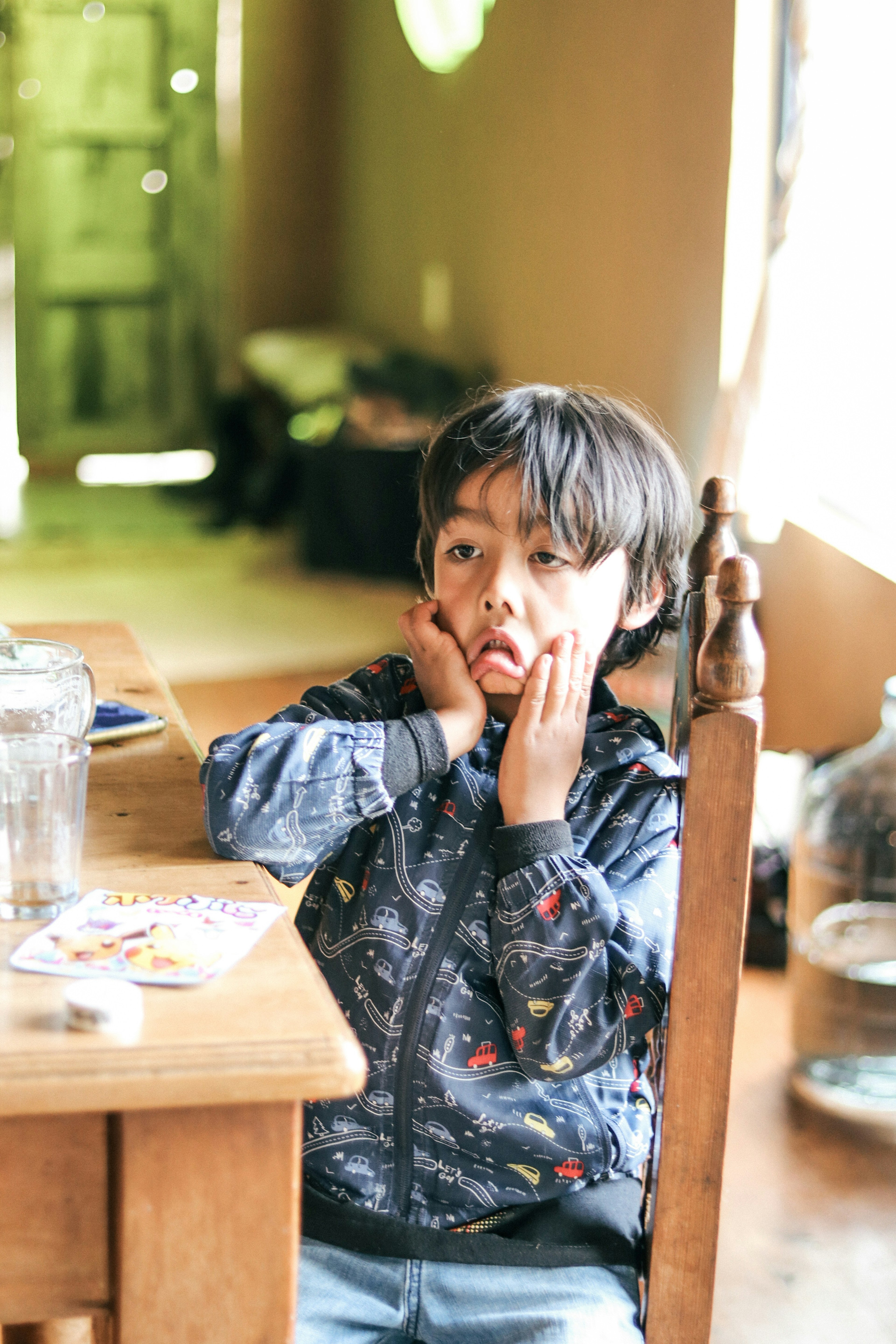 Niño sentado en una mesa con una expresión interesante apoyando su rostro en las manos