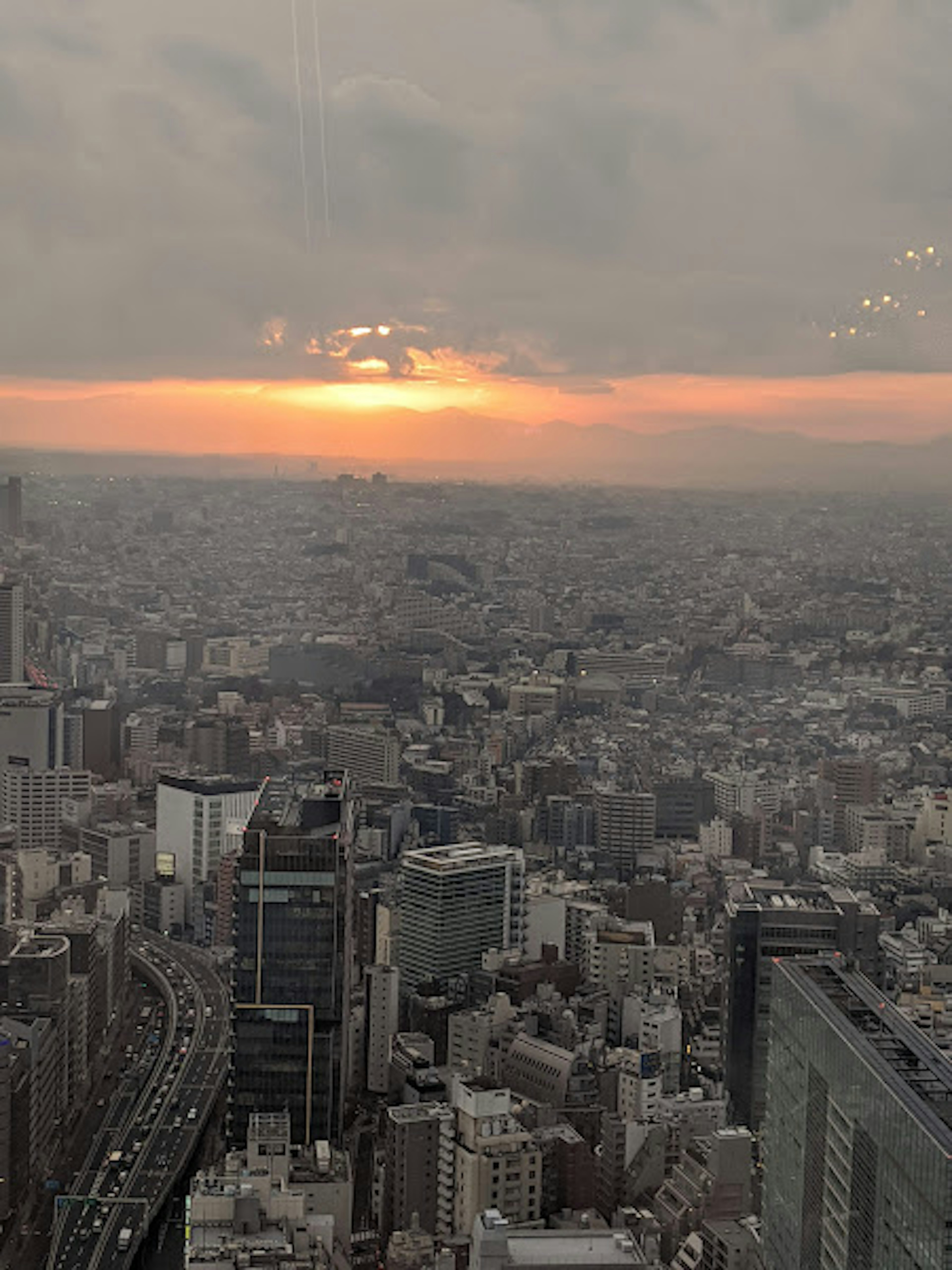 Pemandangan kota Tokyo dengan matahari terbenam di latar belakang menampilkan gedung pencakar langit dan area perkotaan yang luas