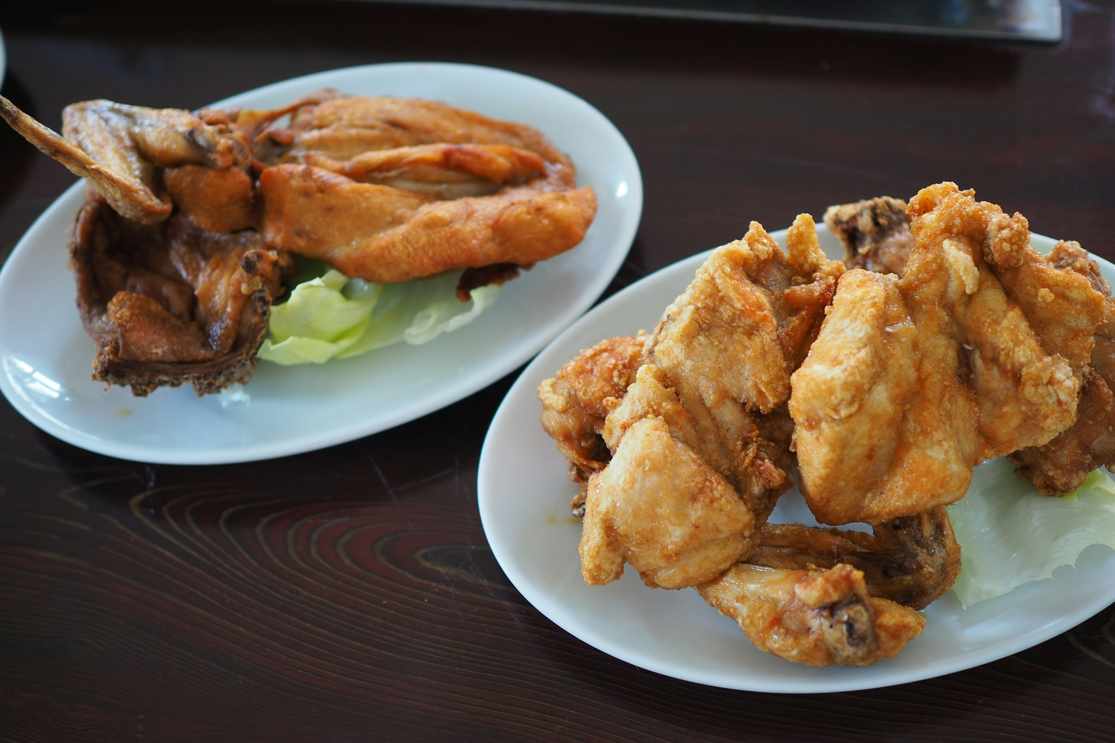 Dua piring ayam goreng, satu dengan potongan utuh dan yang lainnya dengan berbagai potongan di atas selada