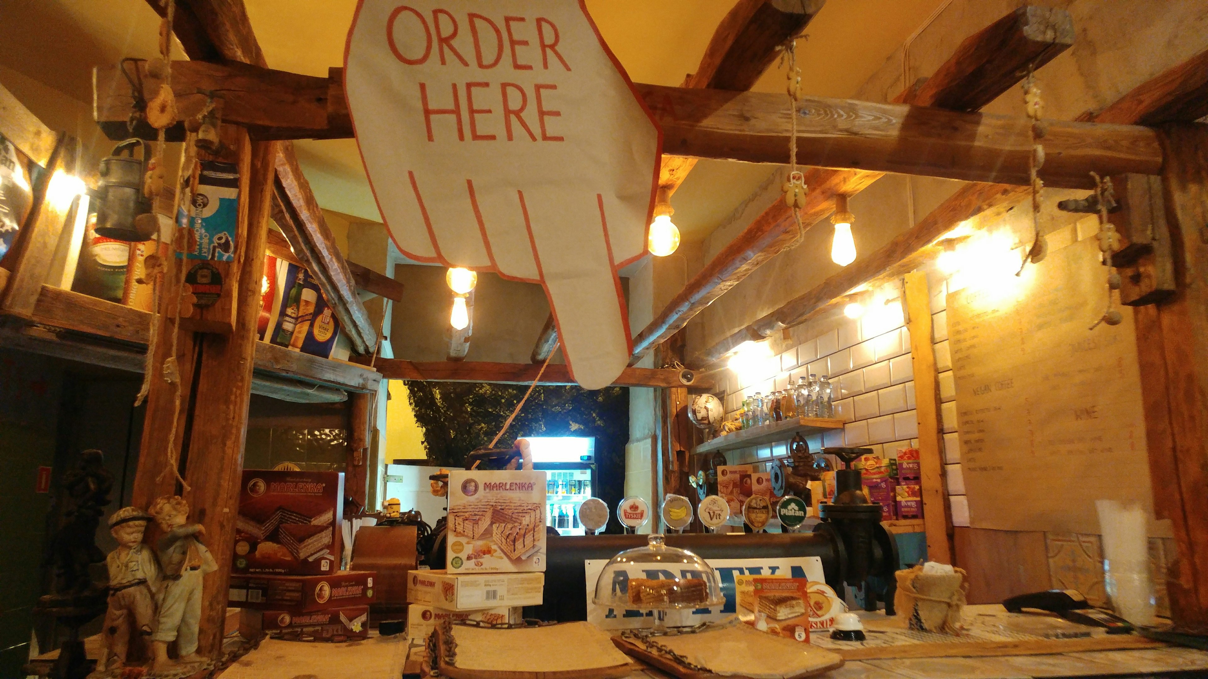 Interior of a cafe featuring a large wooden sign that says 'ORDER HERE' with a hand pointing down