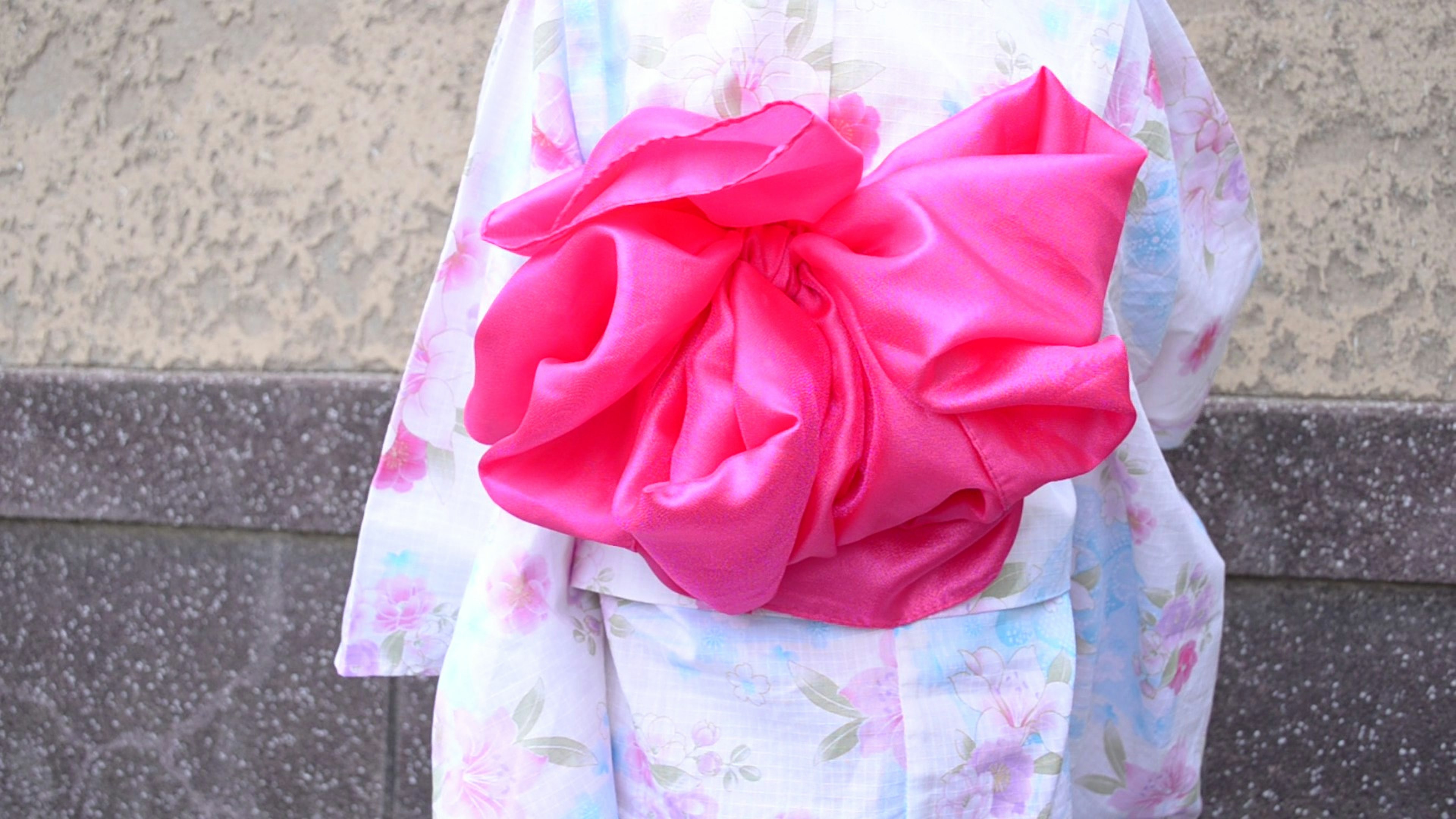 Una mujer con un kimono de color claro y un gran lazo obi rosa