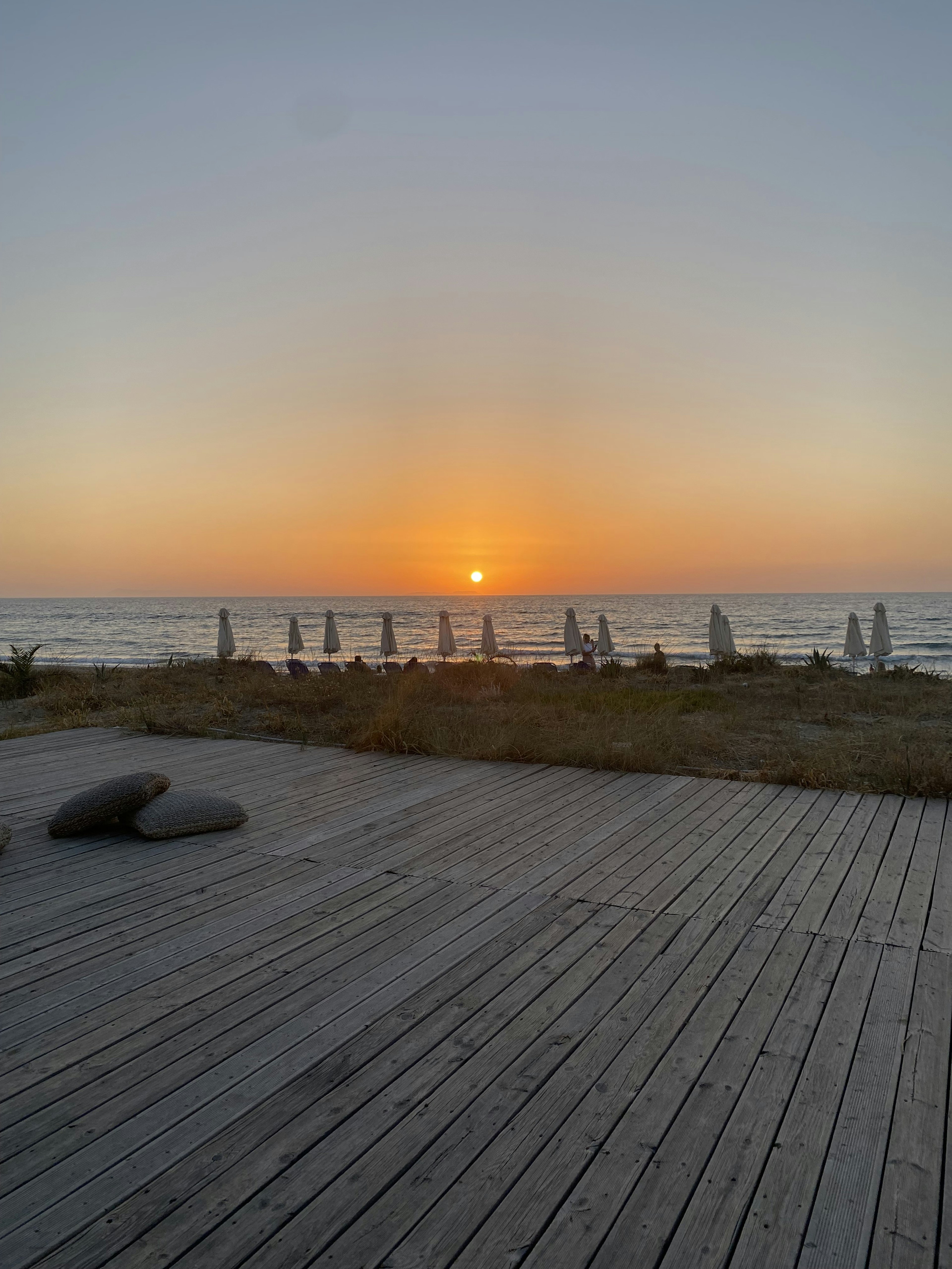 Coucher de soleil sur l'océan avec une terrasse en bois et des parasols alignés