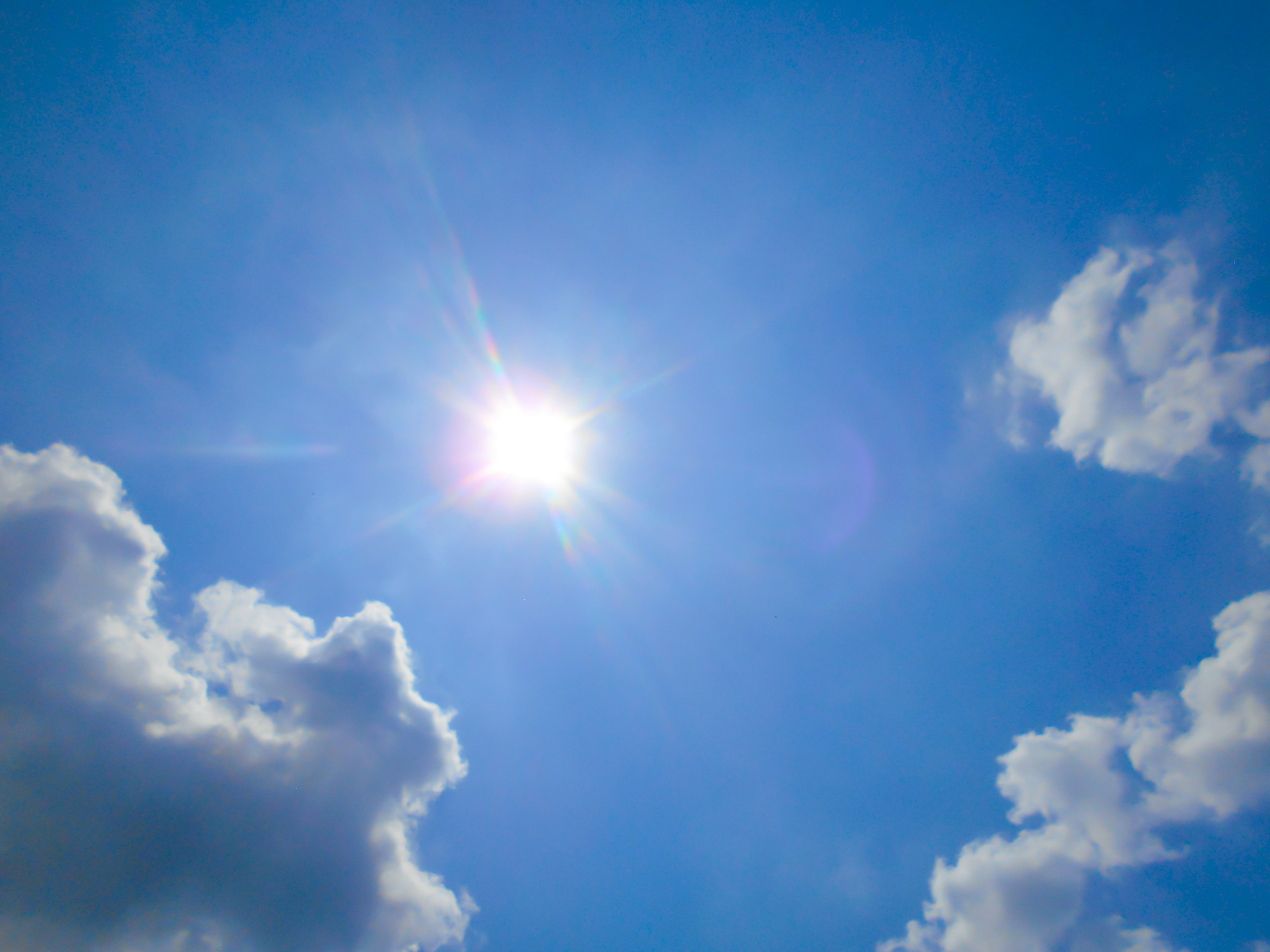 Bright sun in a clear blue sky with fluffy clouds