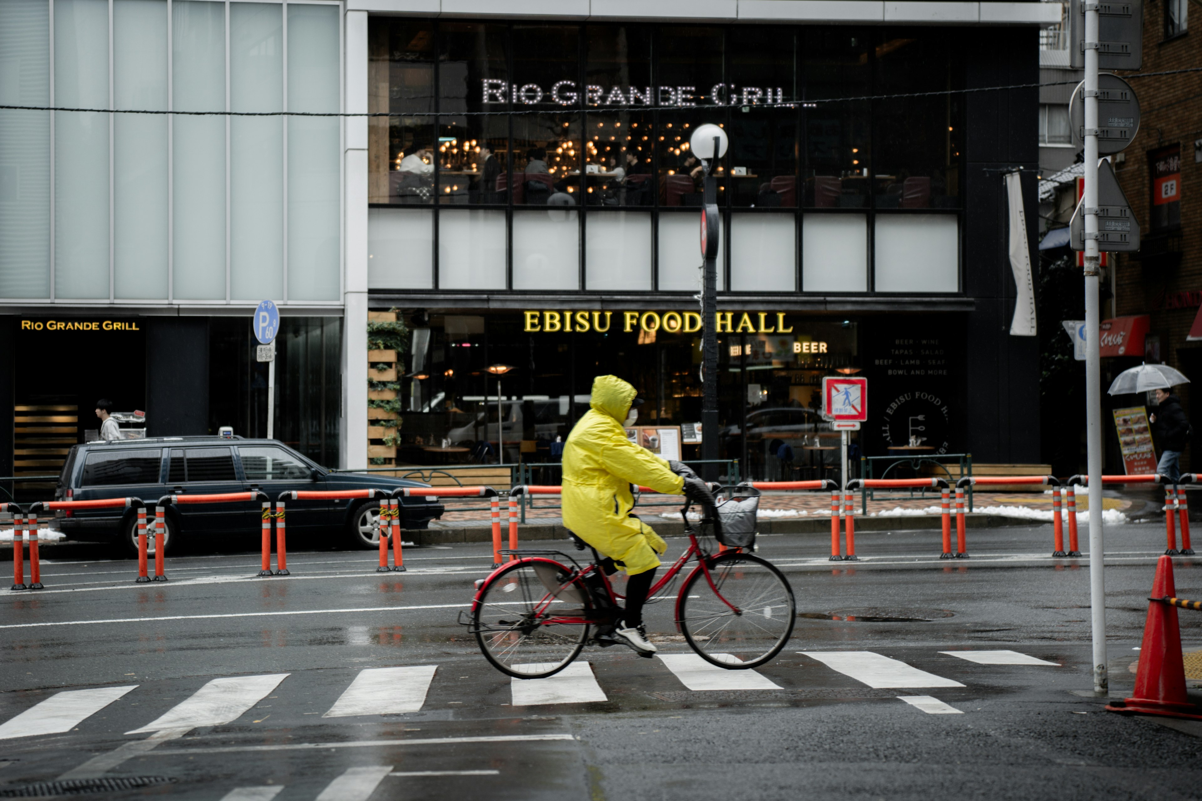 Ein Radfahrer in einem gelben Regenmantel, der an einem regnerischen Tag die Straße in der Stadt überquert