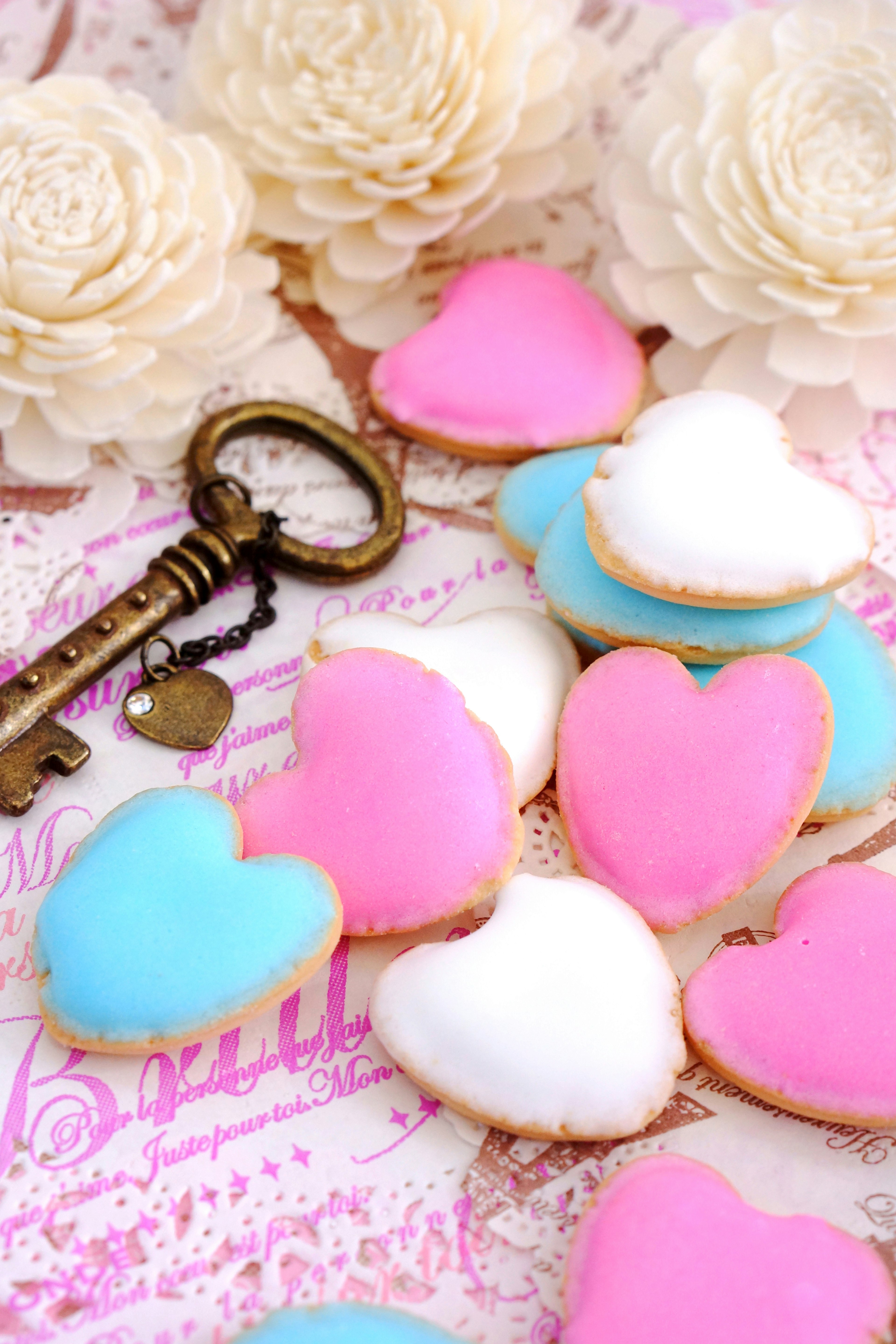 Biscuits en forme de cœur décorés de glaçage bleu, rose et blanc sur un fond floral