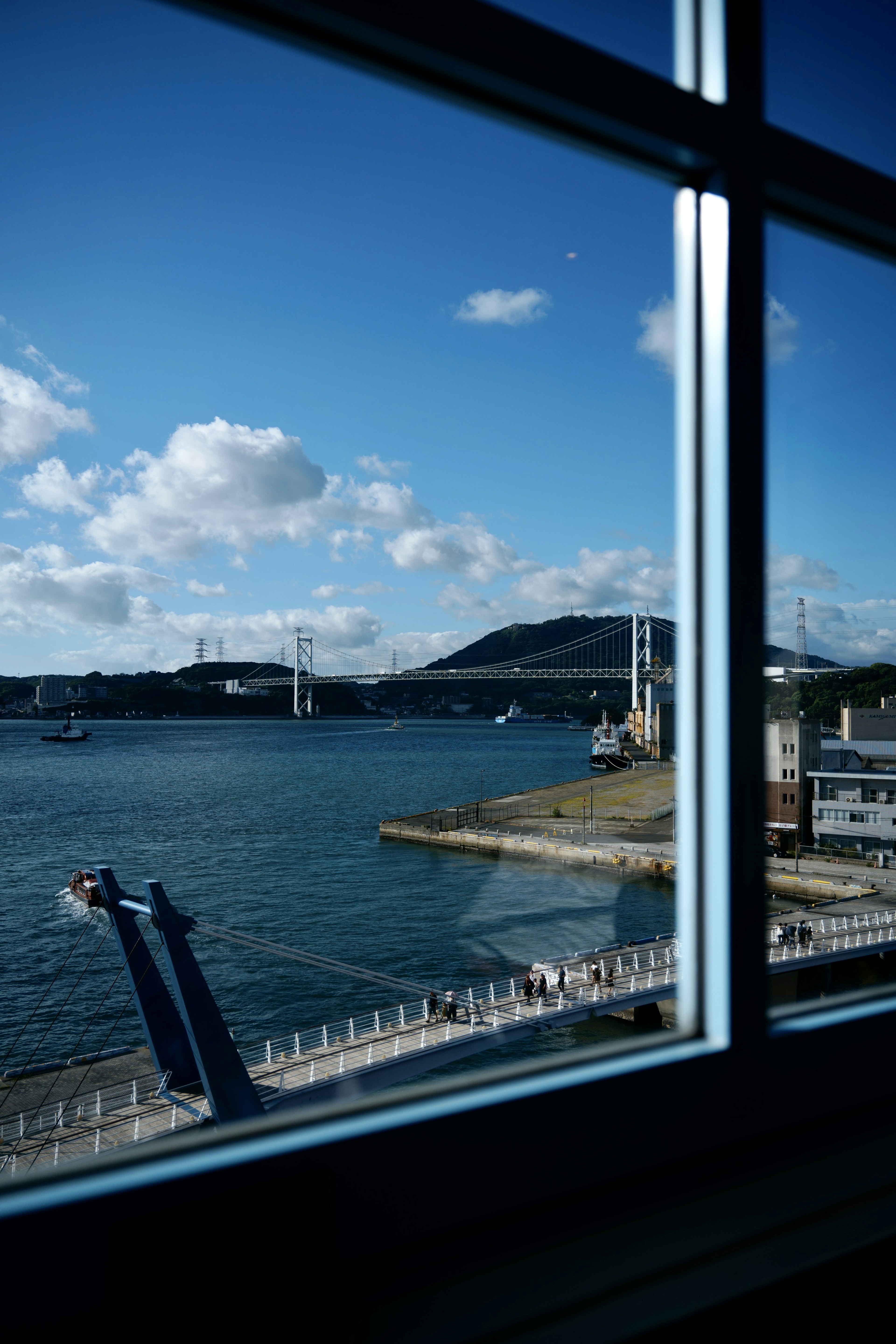 Blick auf einen Hafen mit blauem Himmel und weißen Wolken durch ein Fenster