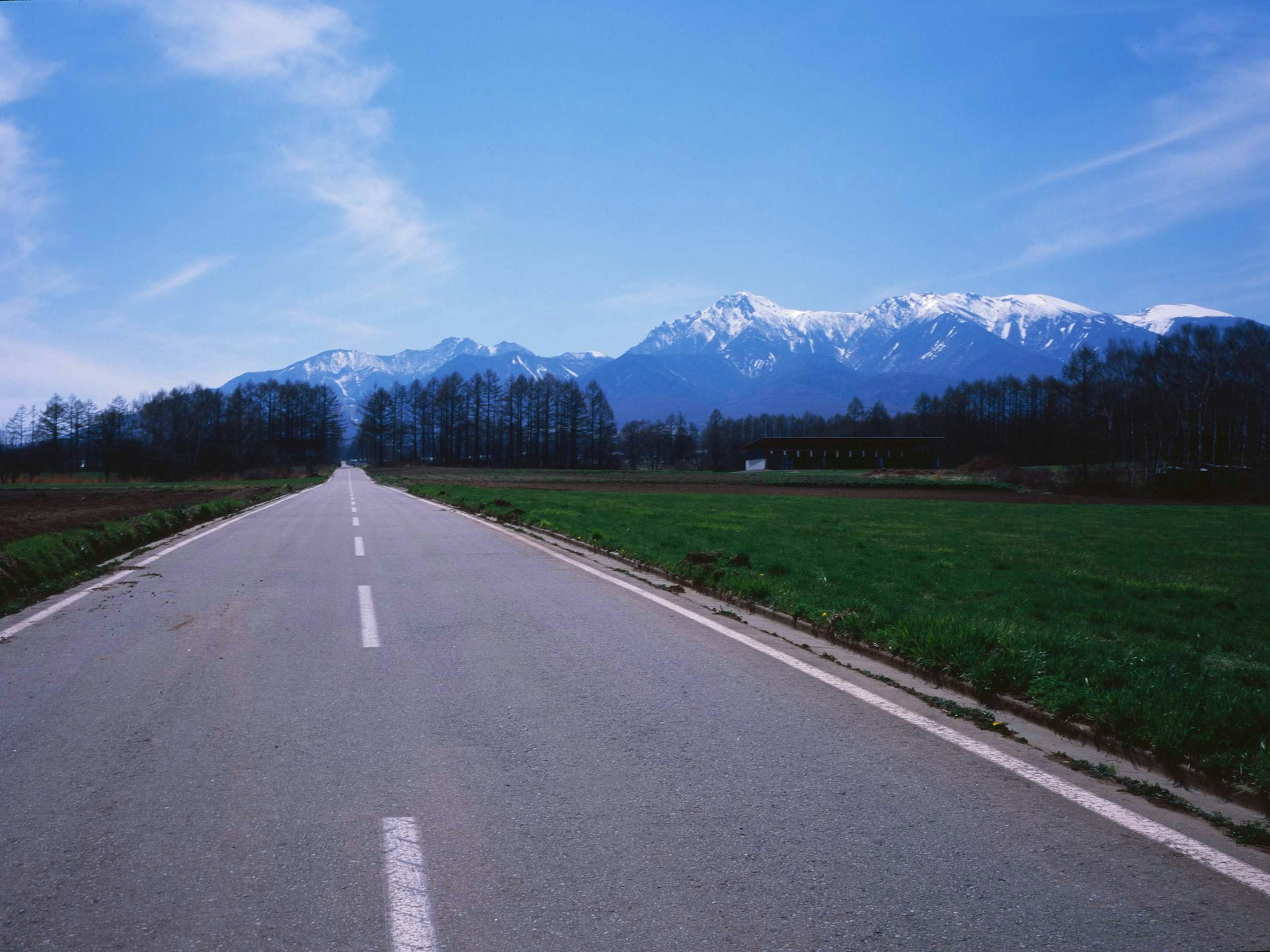 青空の下に広がる山々と緑の田園風景の中の直線道路