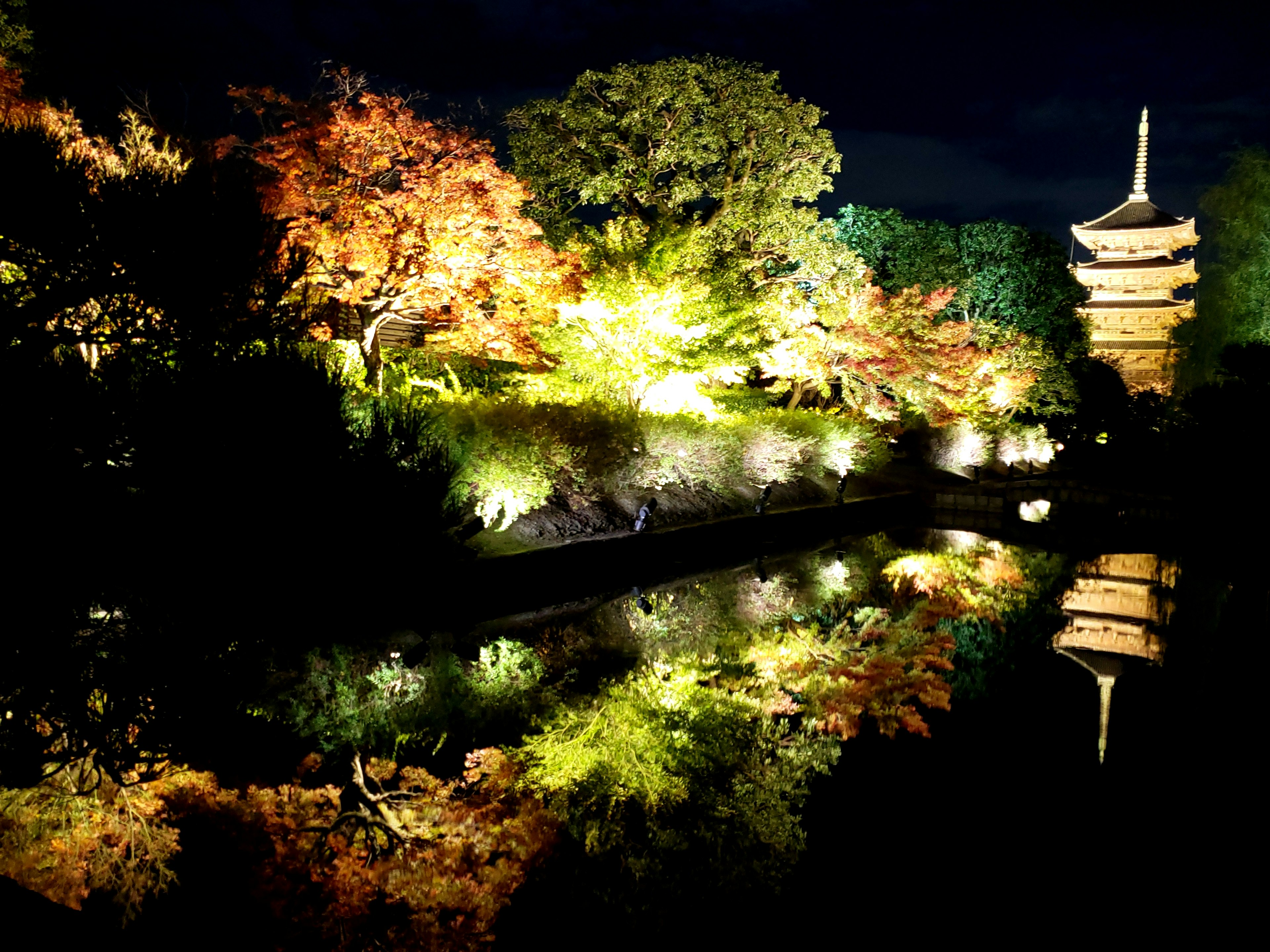 Schöne Nachtansicht eines japanischen Gartens mit beleuchtetem Herbstlaub und einer Pagode, die sich im Teich spiegelt