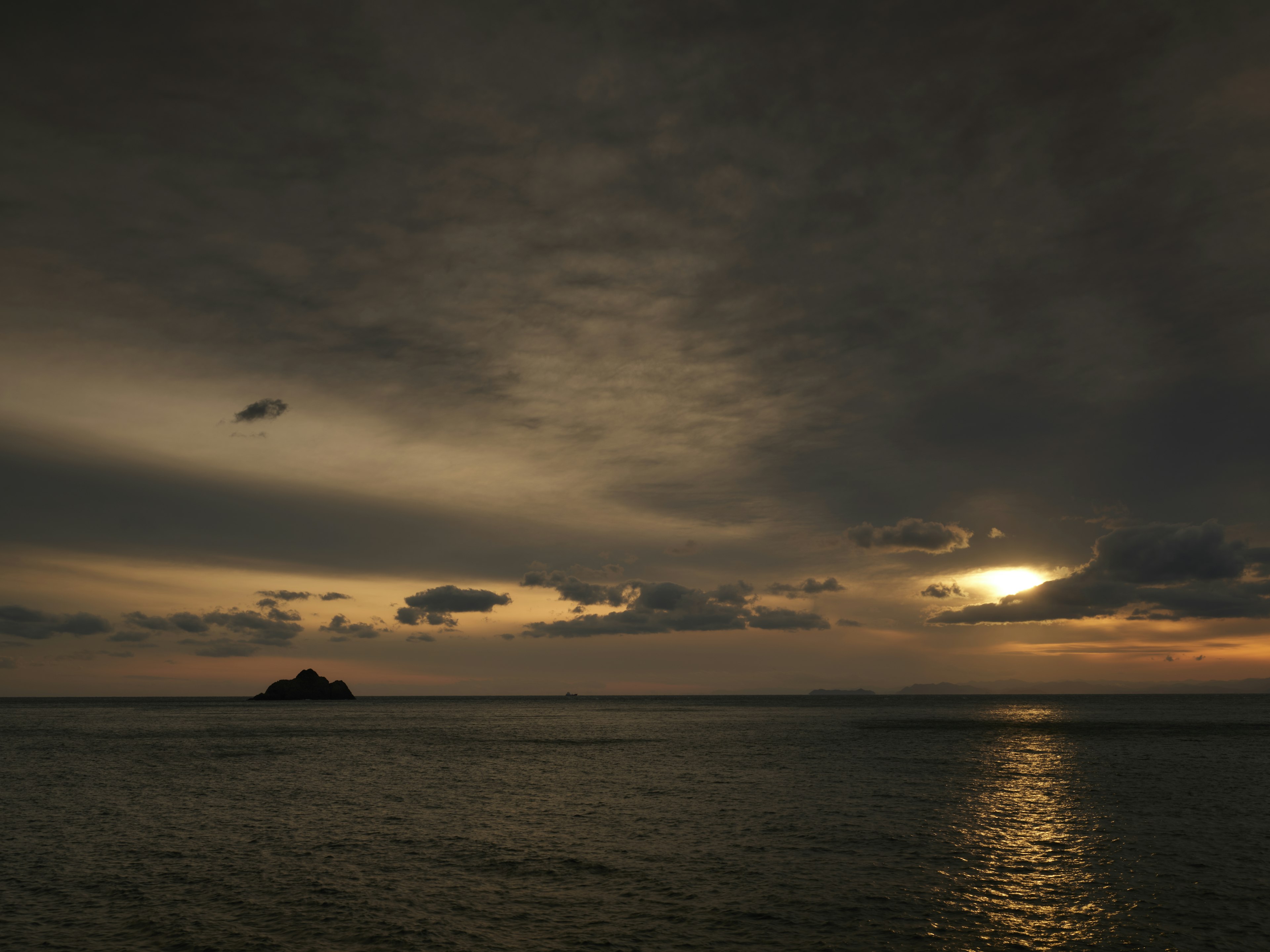 Pemandangan laut dramatis dengan langit gelap dan matahari terbenam yang memantul di air