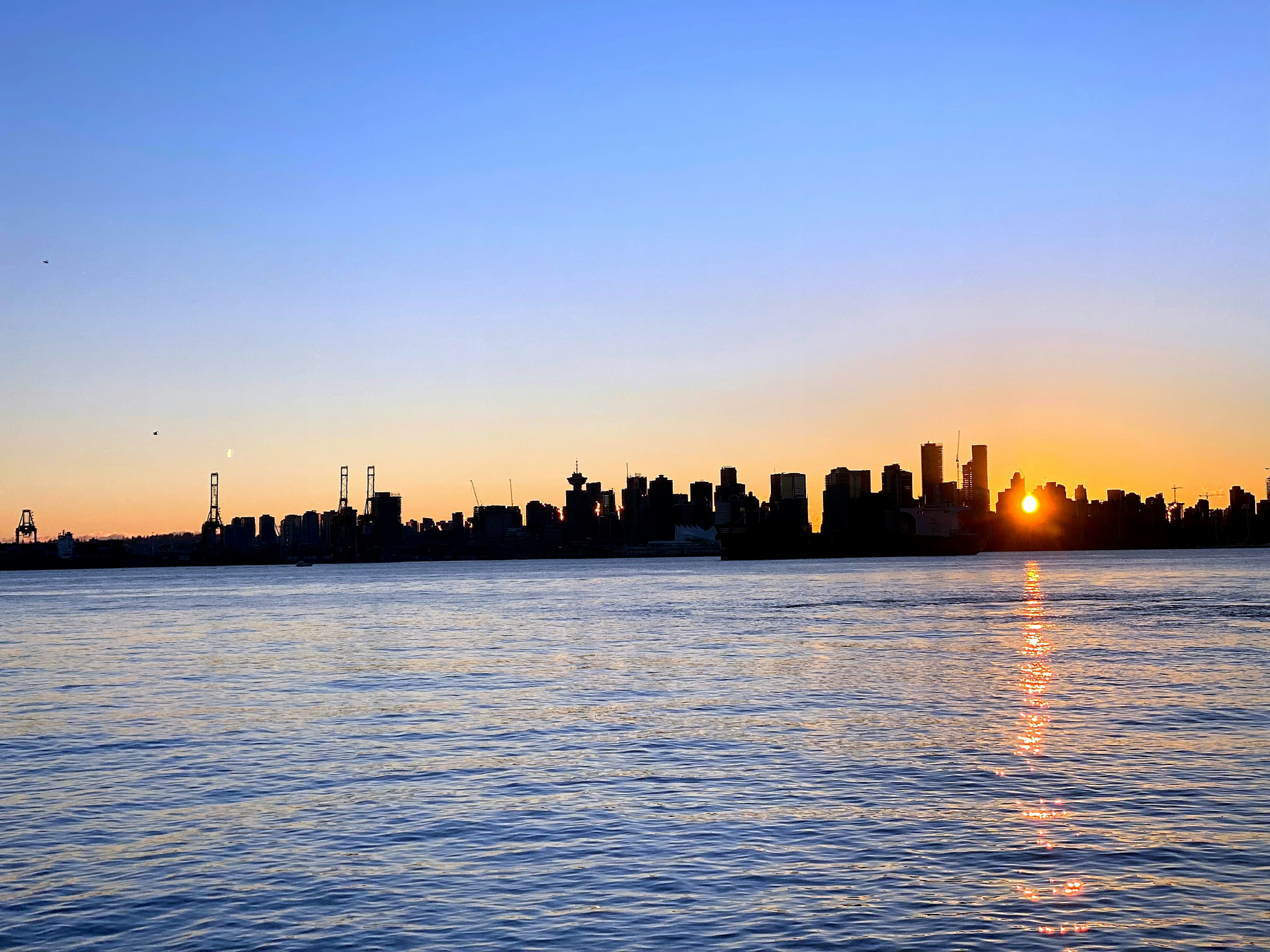 City skyline at sunset with calm water reflecting the colors