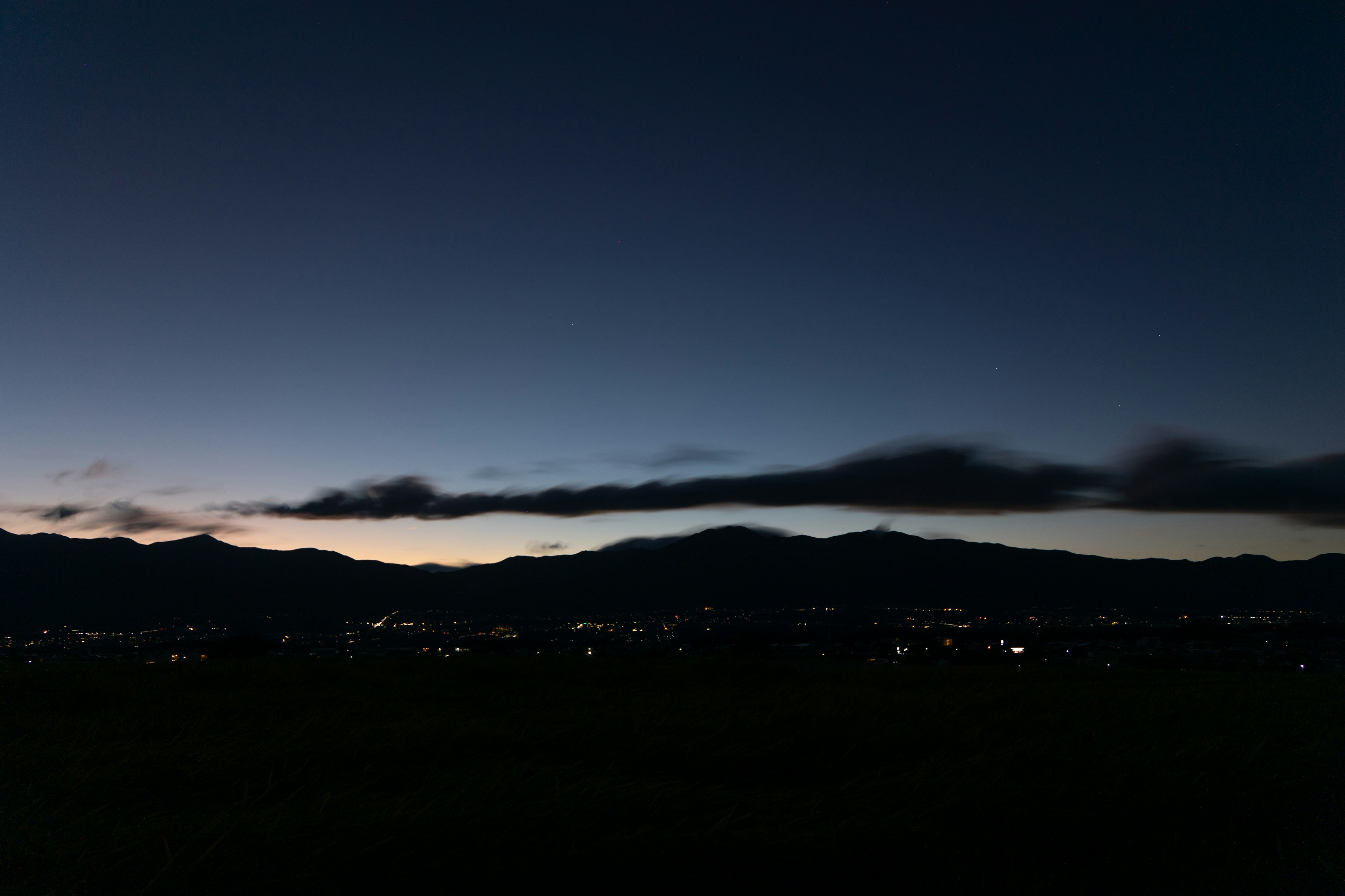 夜明け前の山のシルエットと遠くの街の明かり