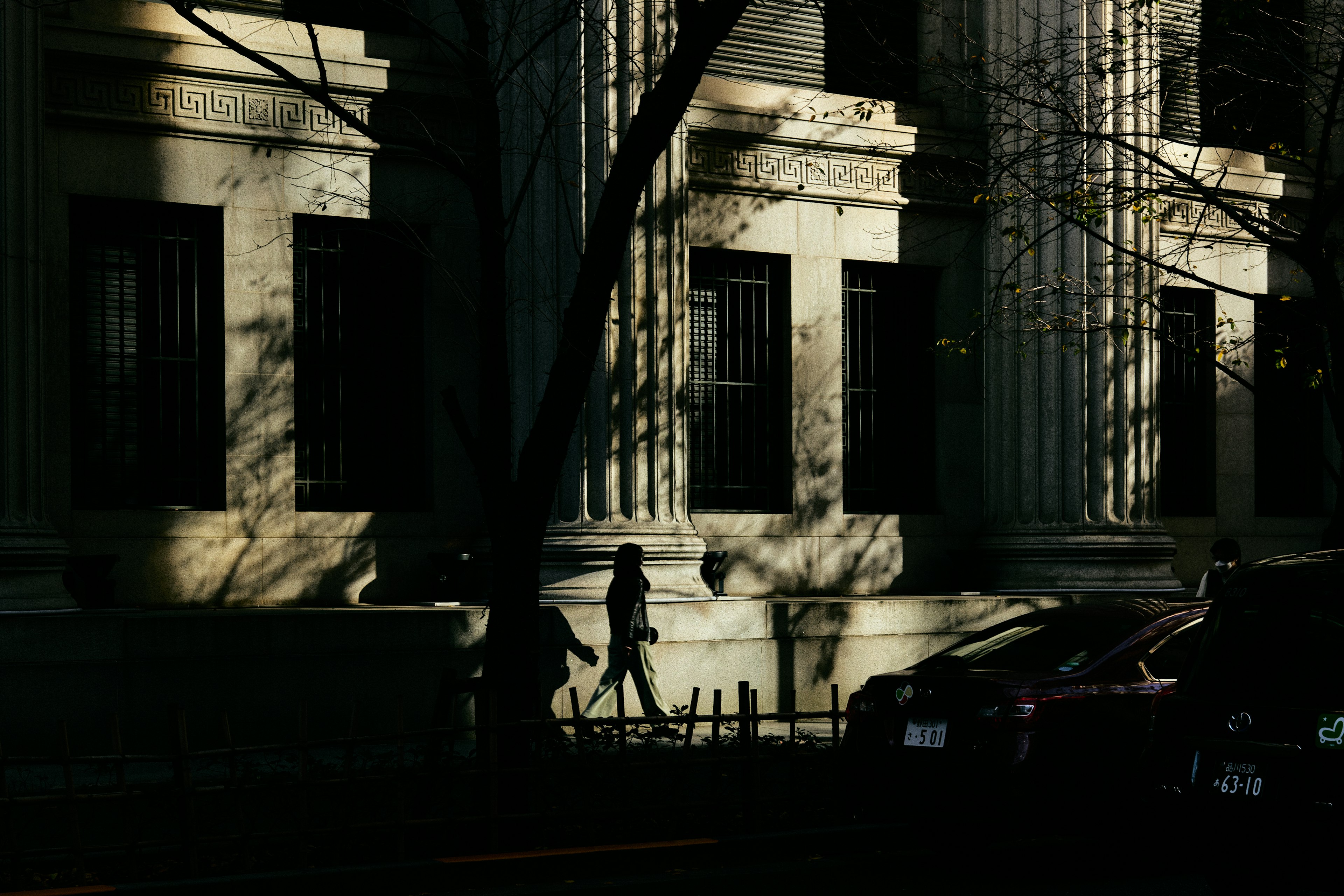 Una persona caminando frente a un edificio clásico con sombras