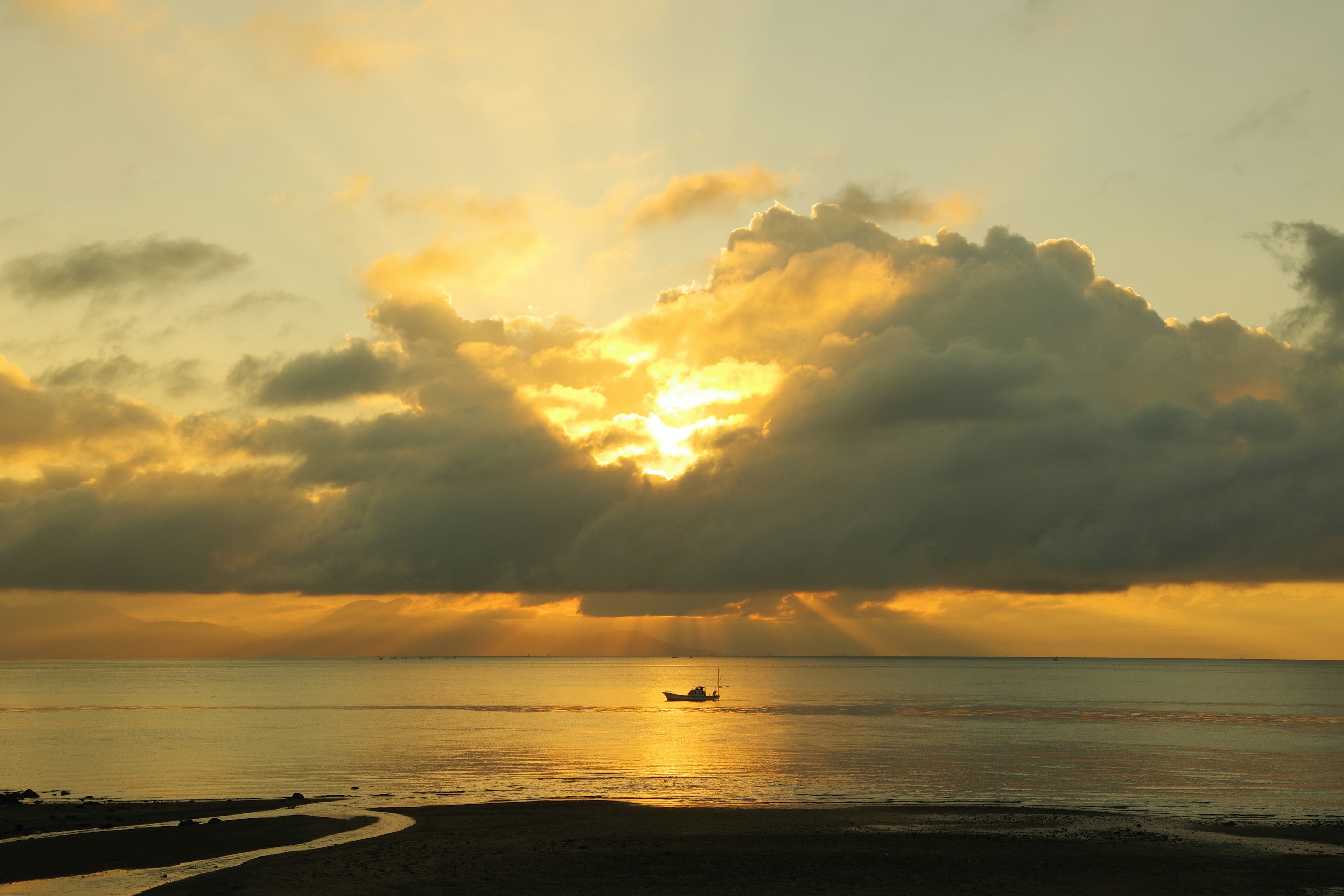 Ein kleines Boot auf einem ruhigen Meer bei Sonnenuntergang mit Lichtstrahlen, die durch die Wolken brechen