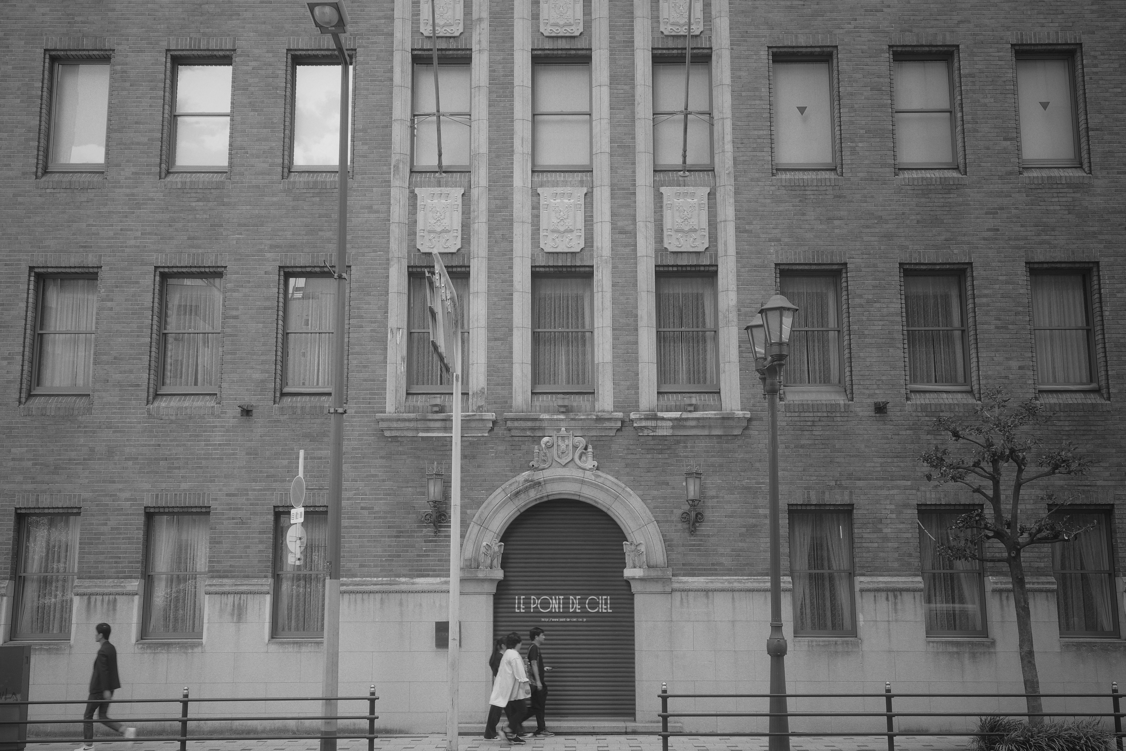 Historic brick building facade with two people walking and a streetlamp