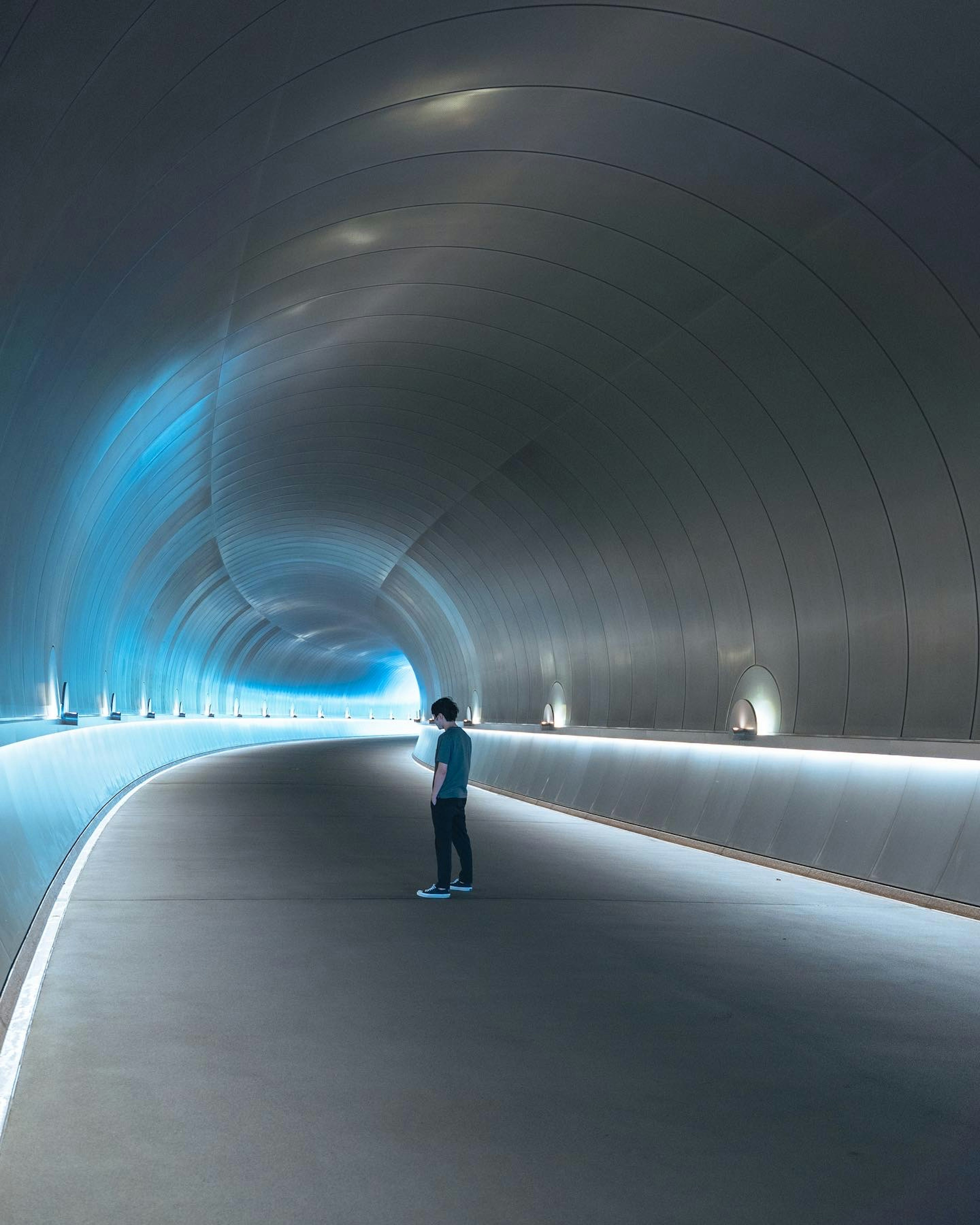 Una persona in piedi in un tunnel liscio illuminato da luce blu