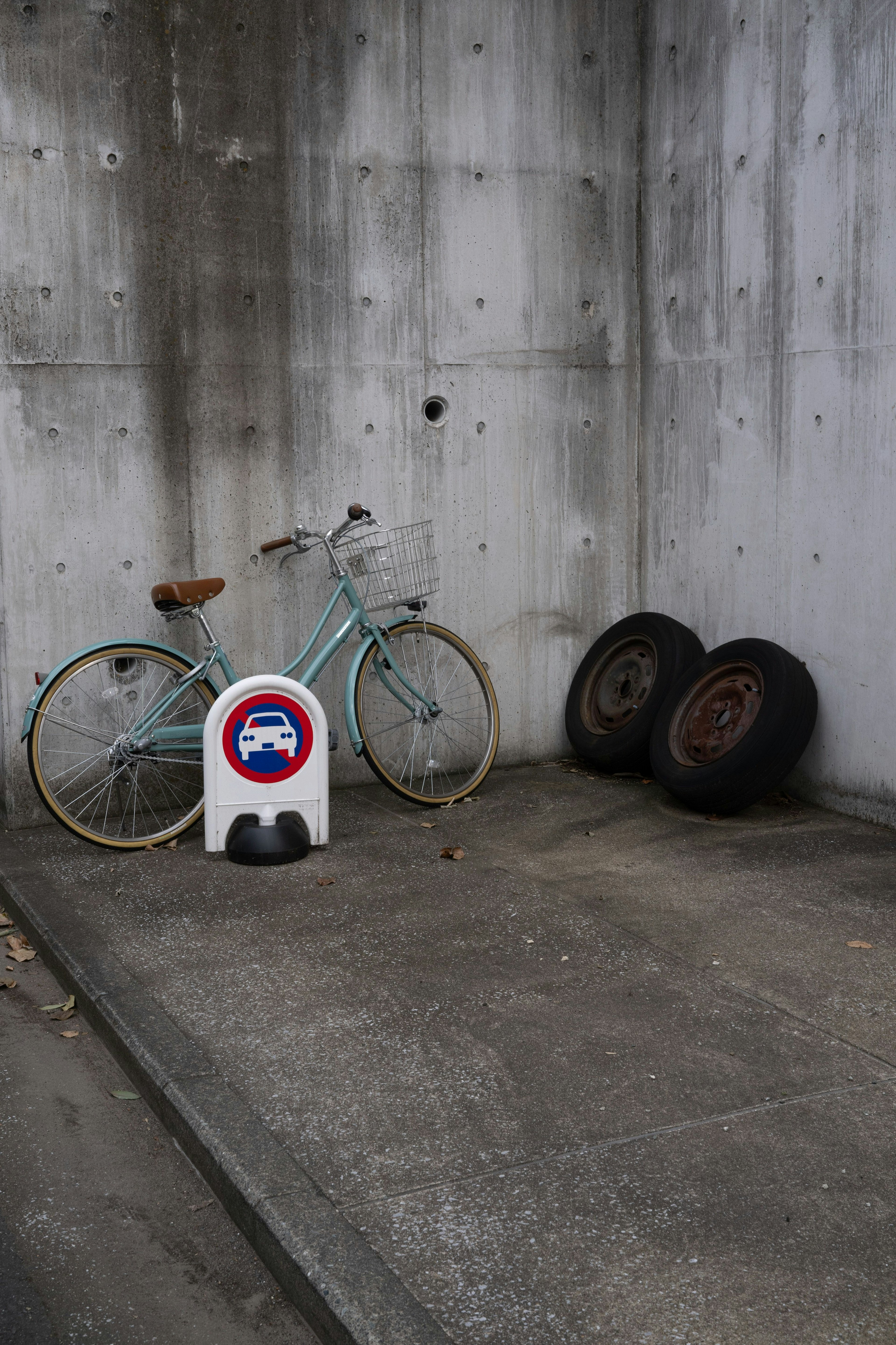 Una bicicletta blu appoggiata a un muro di cemento con due vecchi pneumatici nelle vicinanze