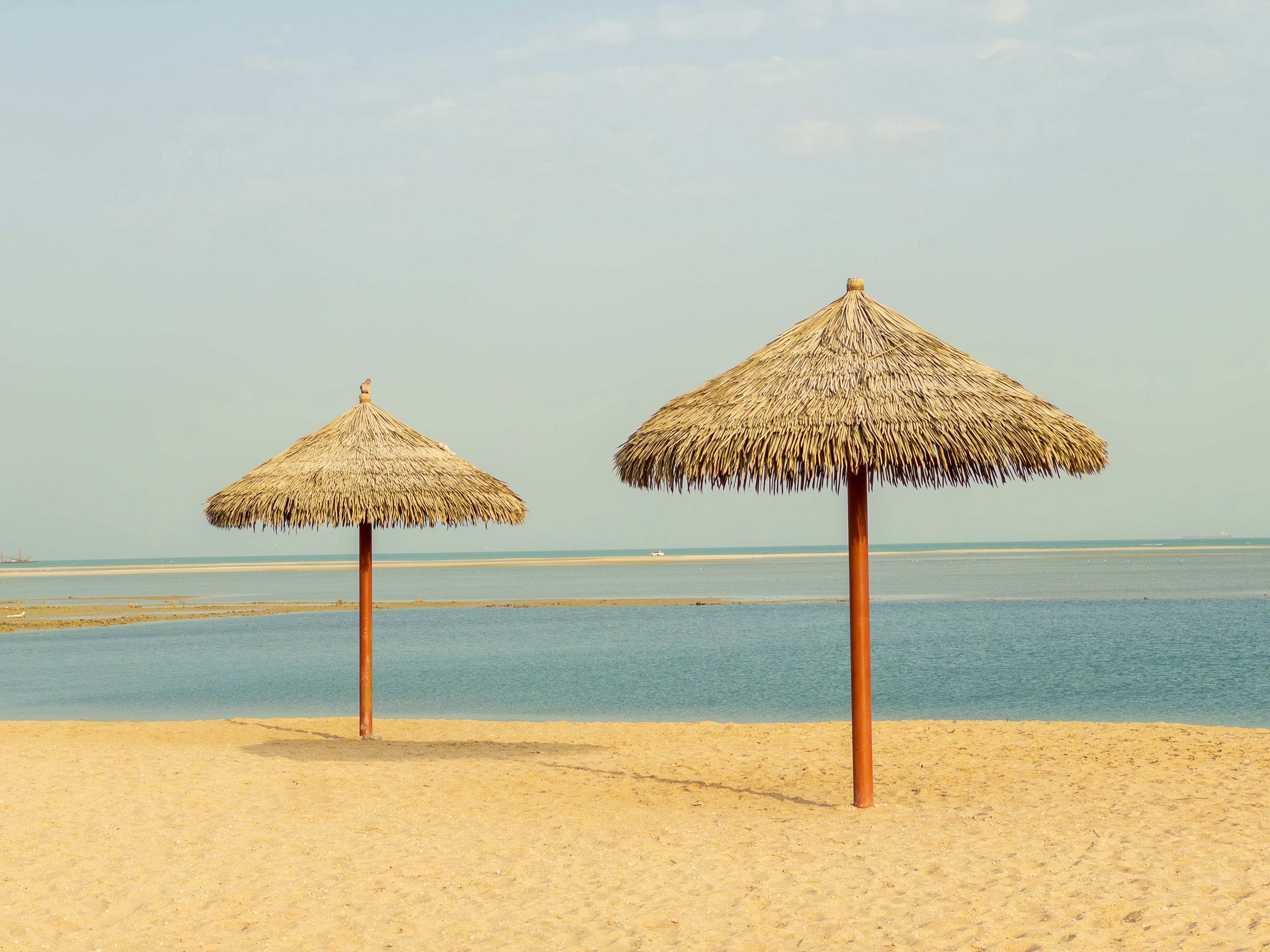 Due ombrelloni di paglia su una spiaggia di sabbia vicino al mare calmo