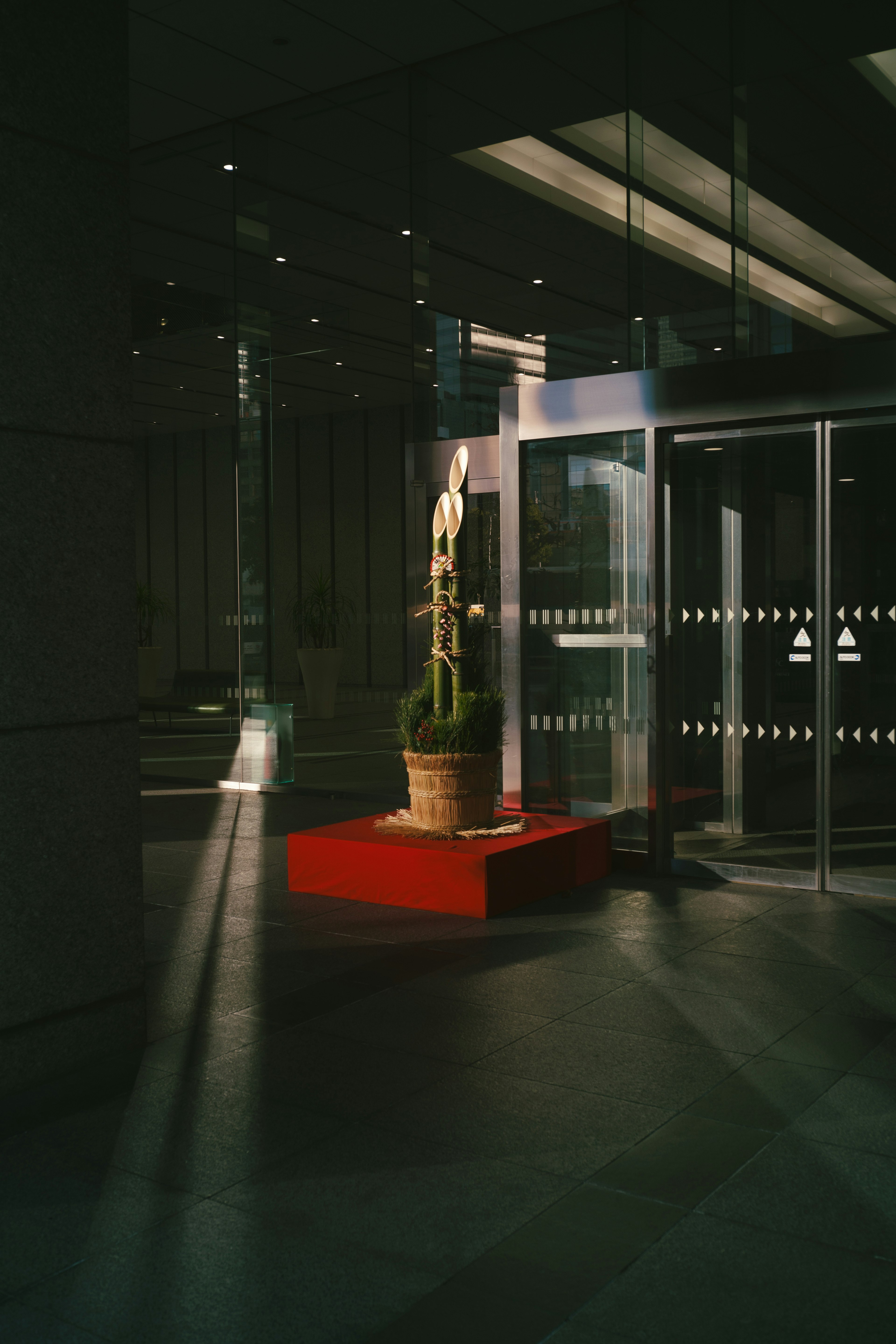 Interior de una entrada moderna con una escultura de planta sobre un pedestal rojo