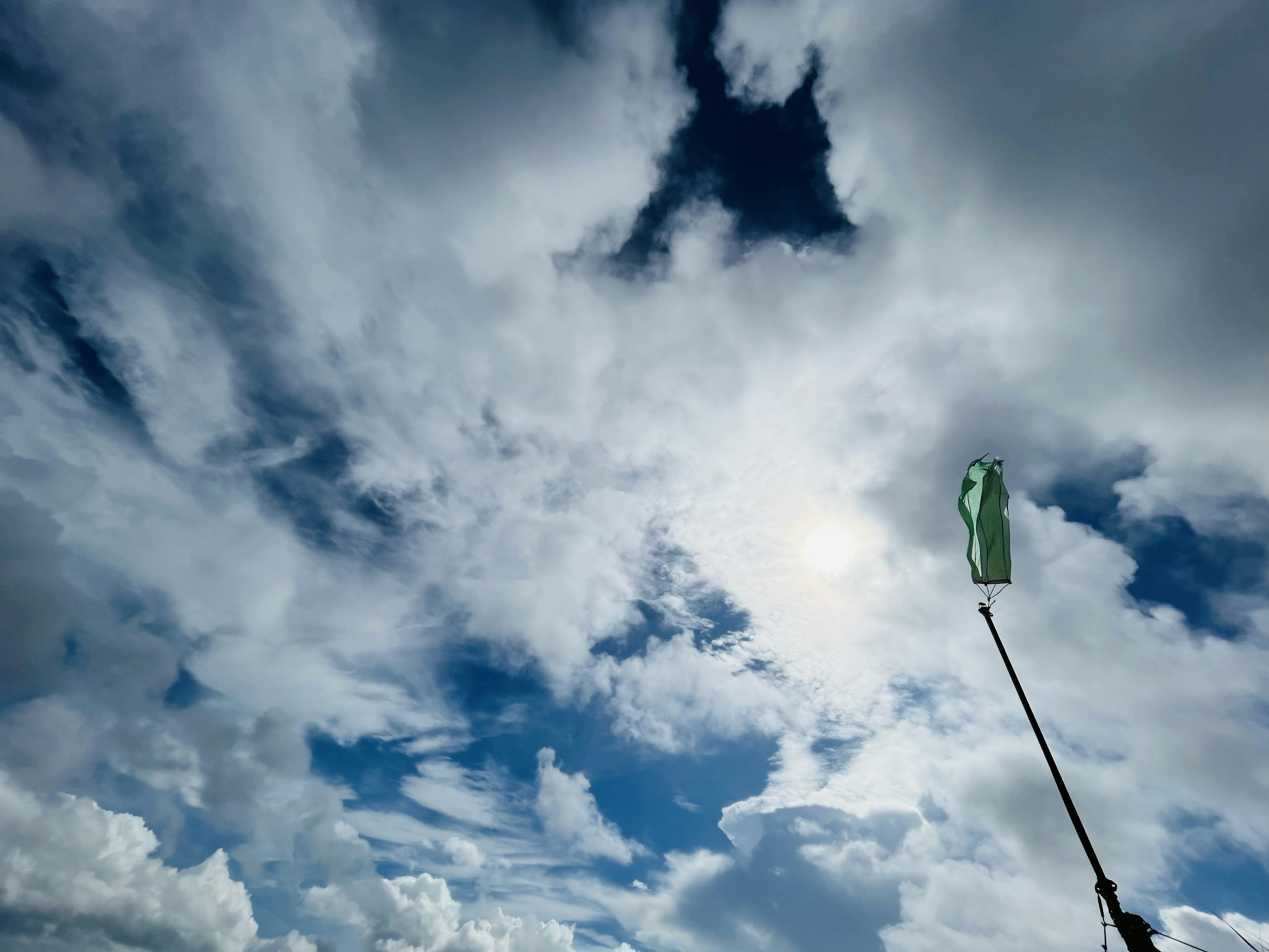 Mano sosteniendo una bandera verde contra un fondo de cielo azul y nubes