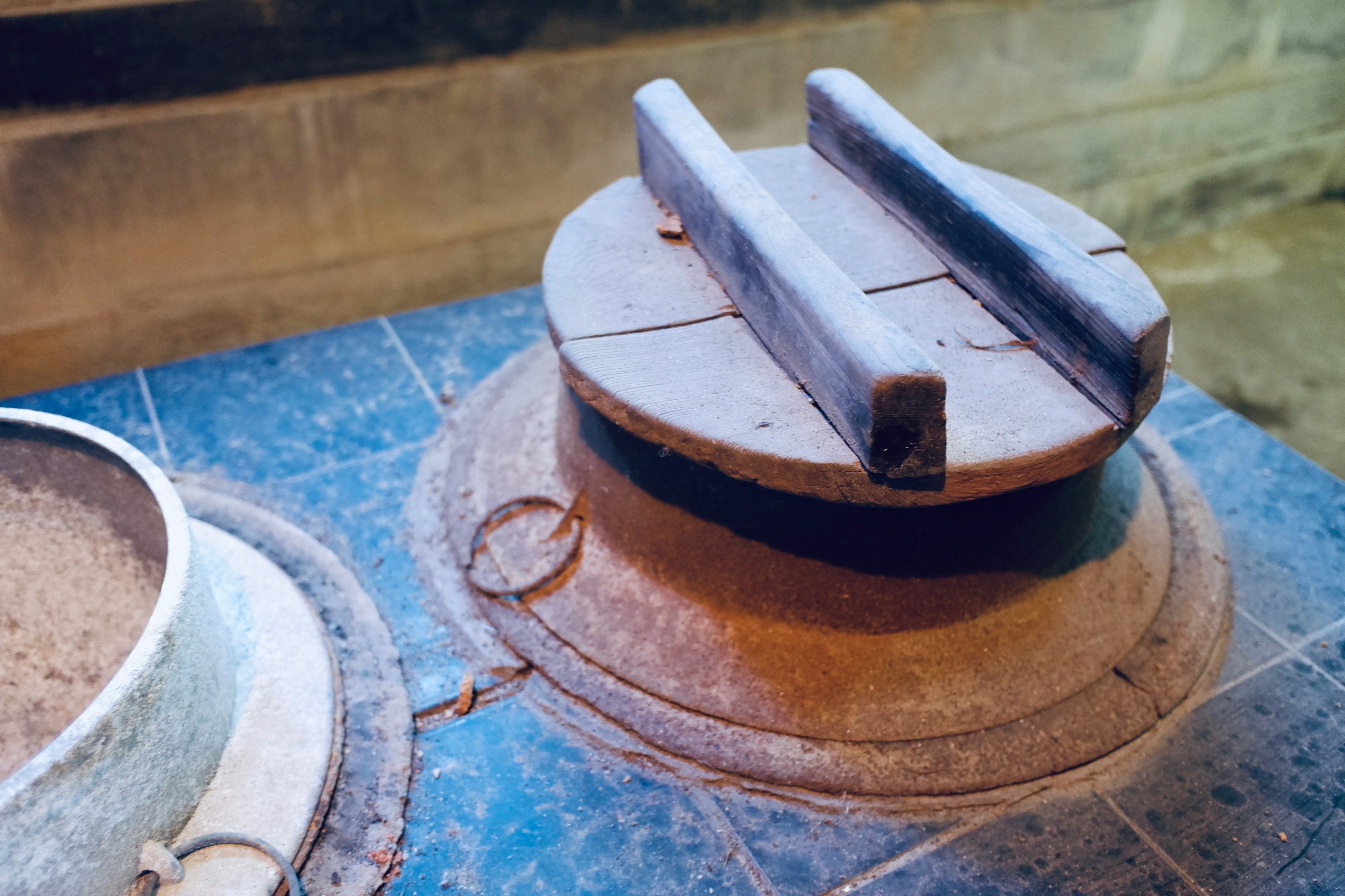 Part of an old cooking device featuring a clay pot lid with wooden handles