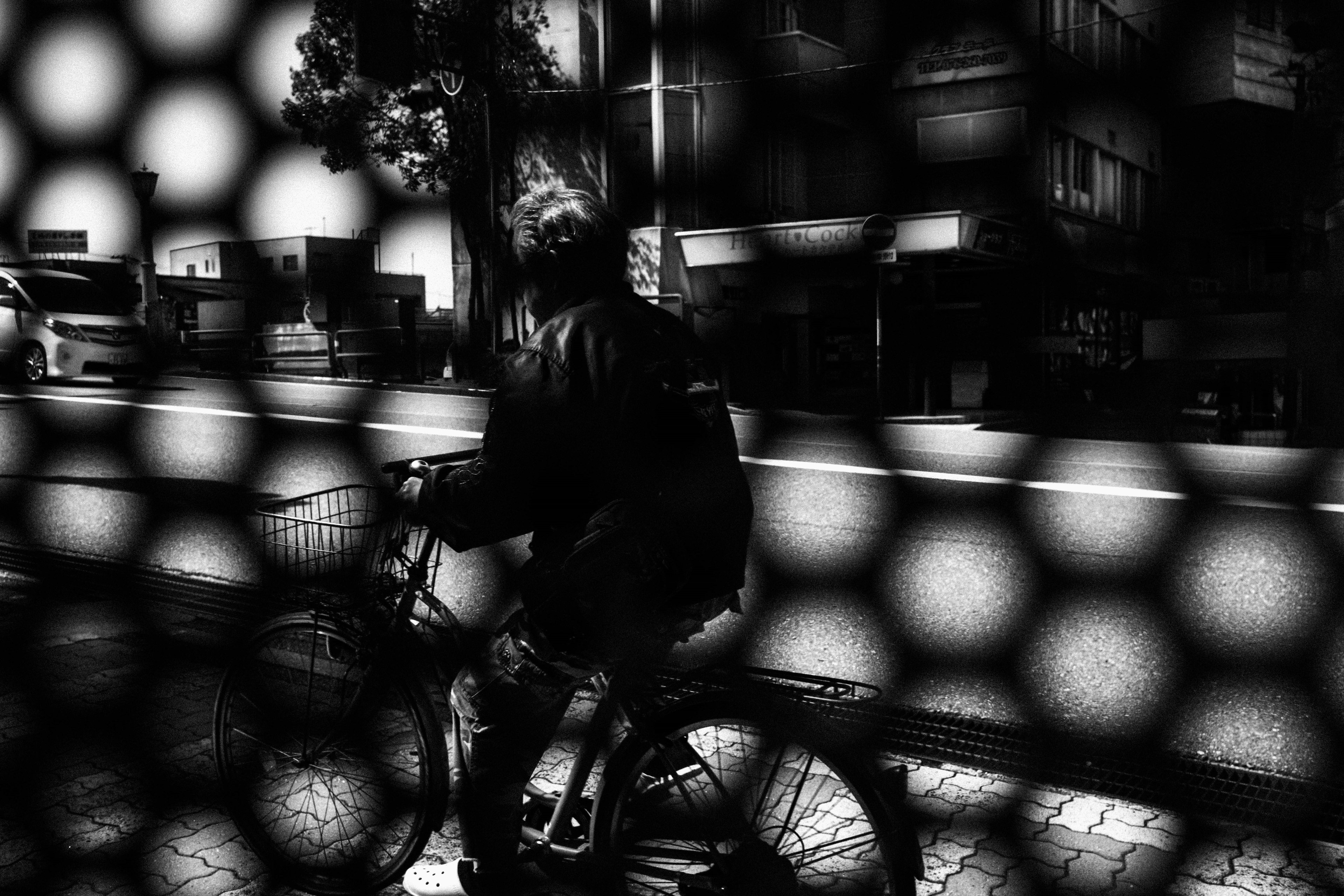 Una foto in bianco e nero di una persona in bicicletta vista attraverso un filtro a rete