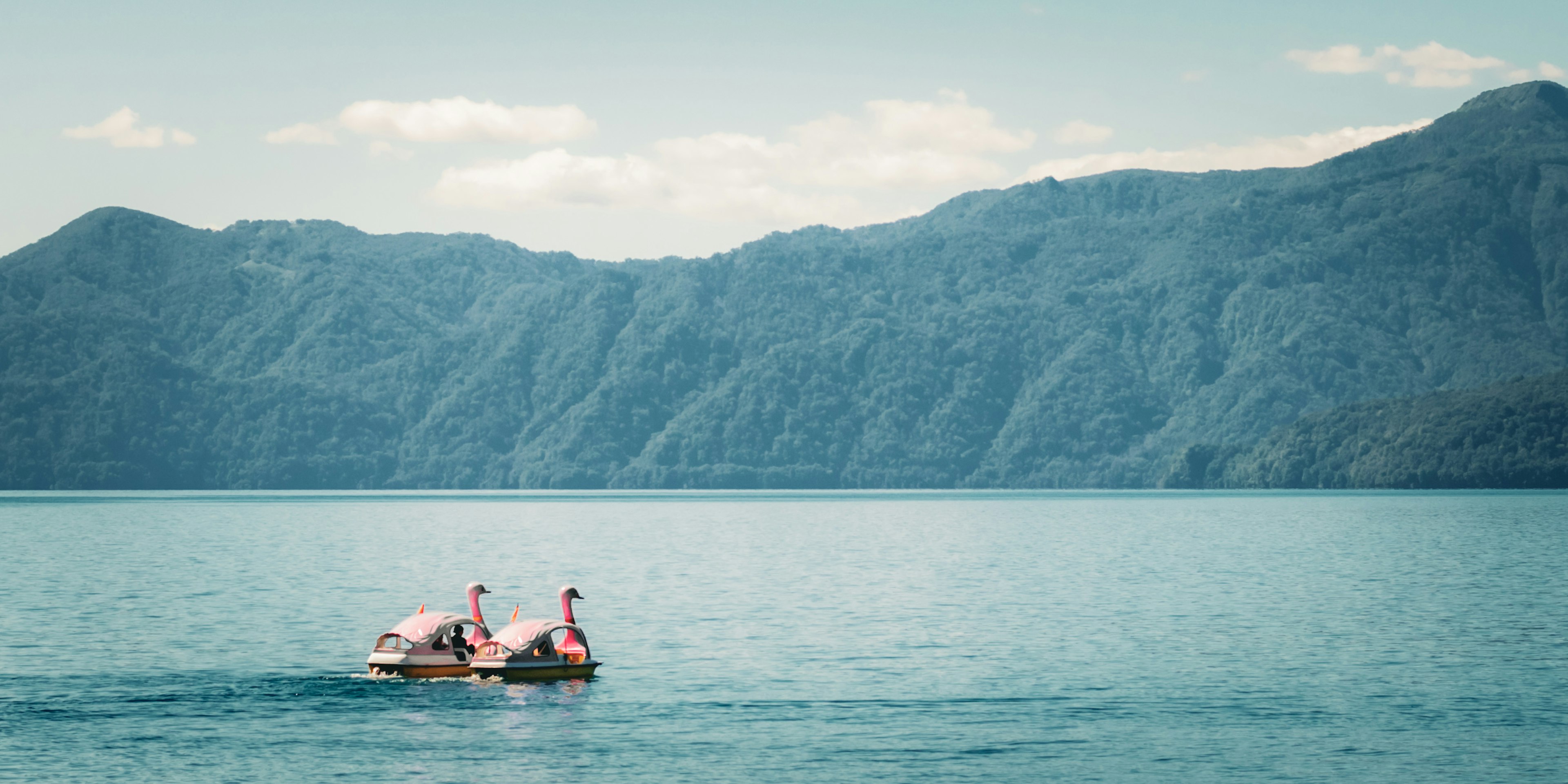 Two people paddling a canoe on a blue lake with mountain backdrop