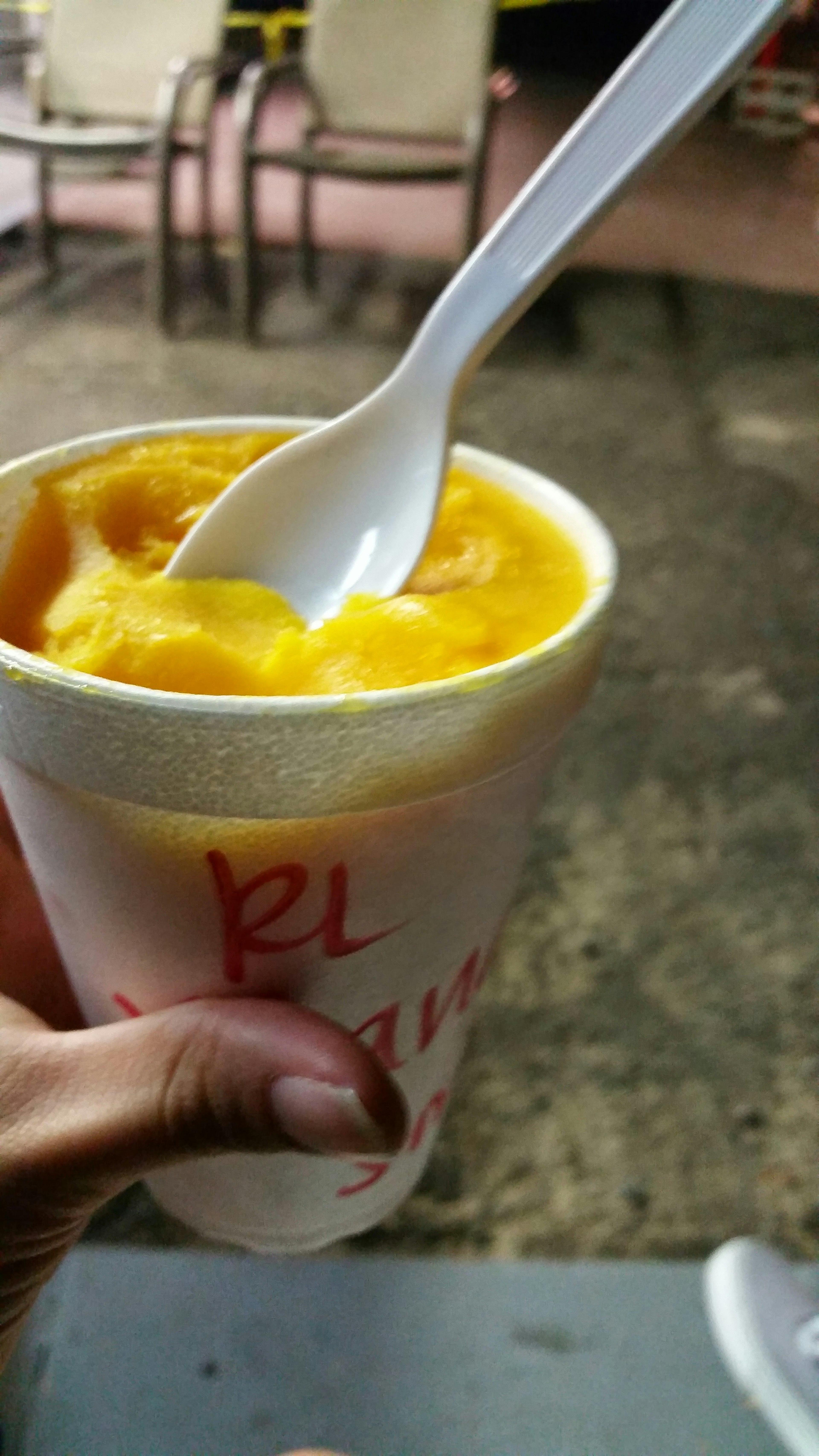 Una taza de helado de mango naranja sostenida en una mano con una cuchara blanca