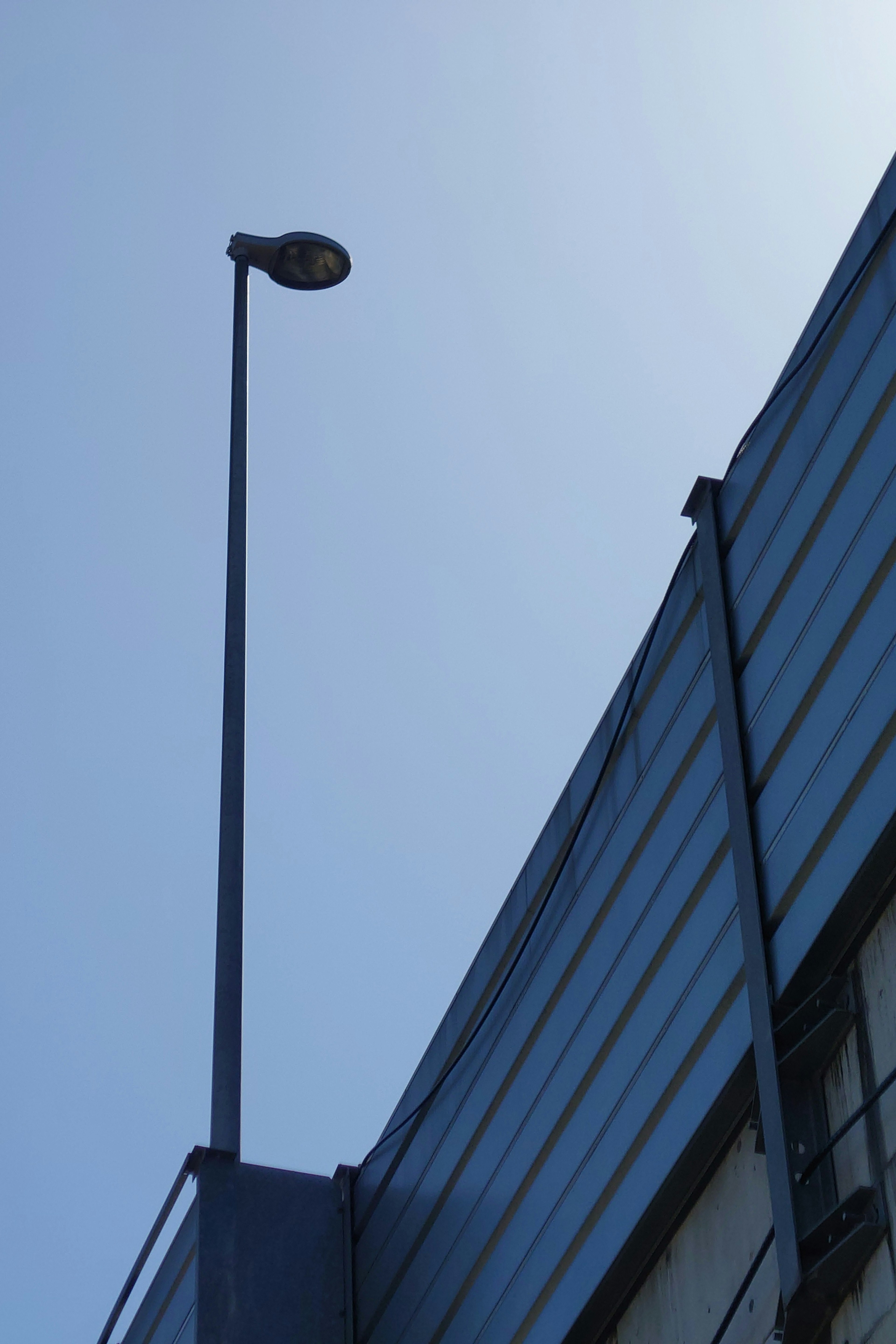 Una farola alta bajo un cielo azul junto a un edificio de vidrio