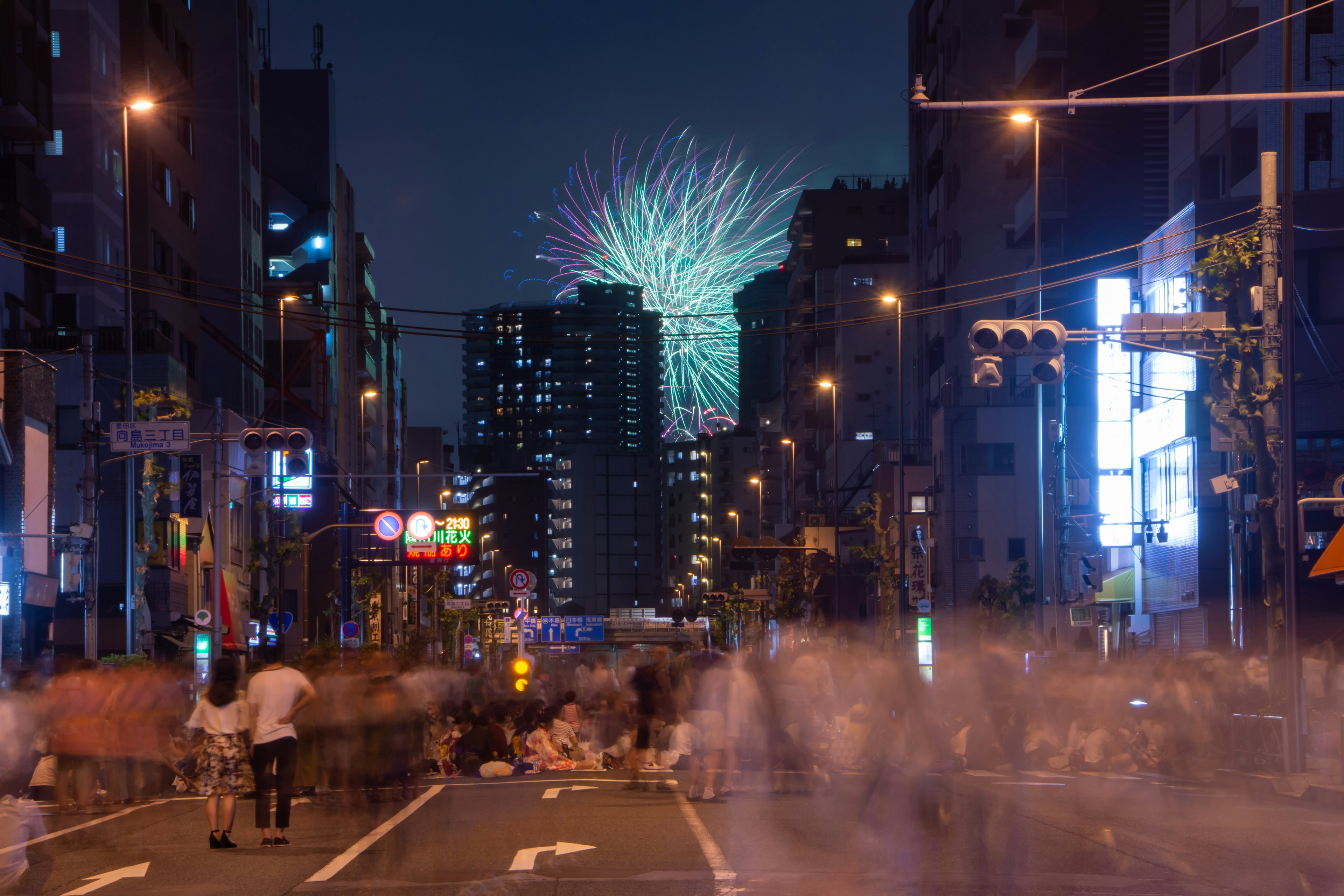 夜の街並みに花火が上がる風景で人々が行き交う様子