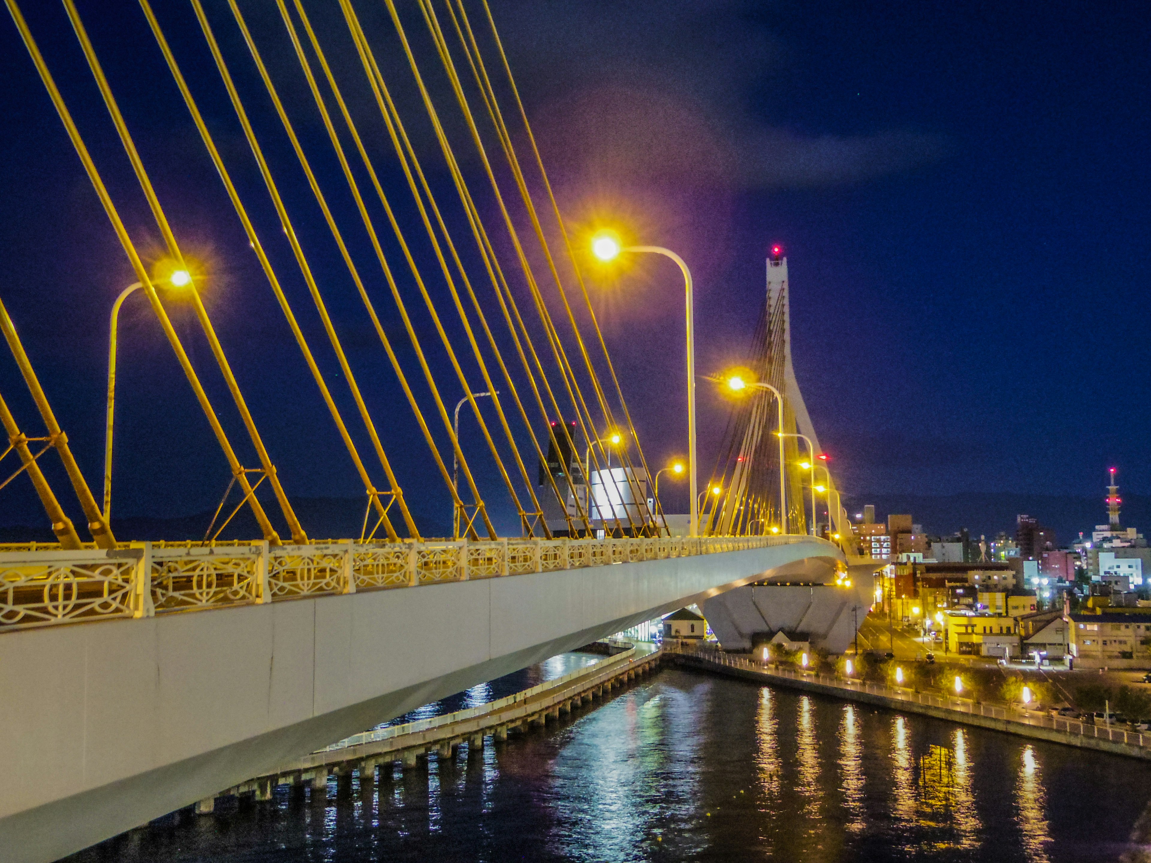 Vista panoramica di un ponte sospeso di notte illuminato da lampioni che si riflettono sull'acqua