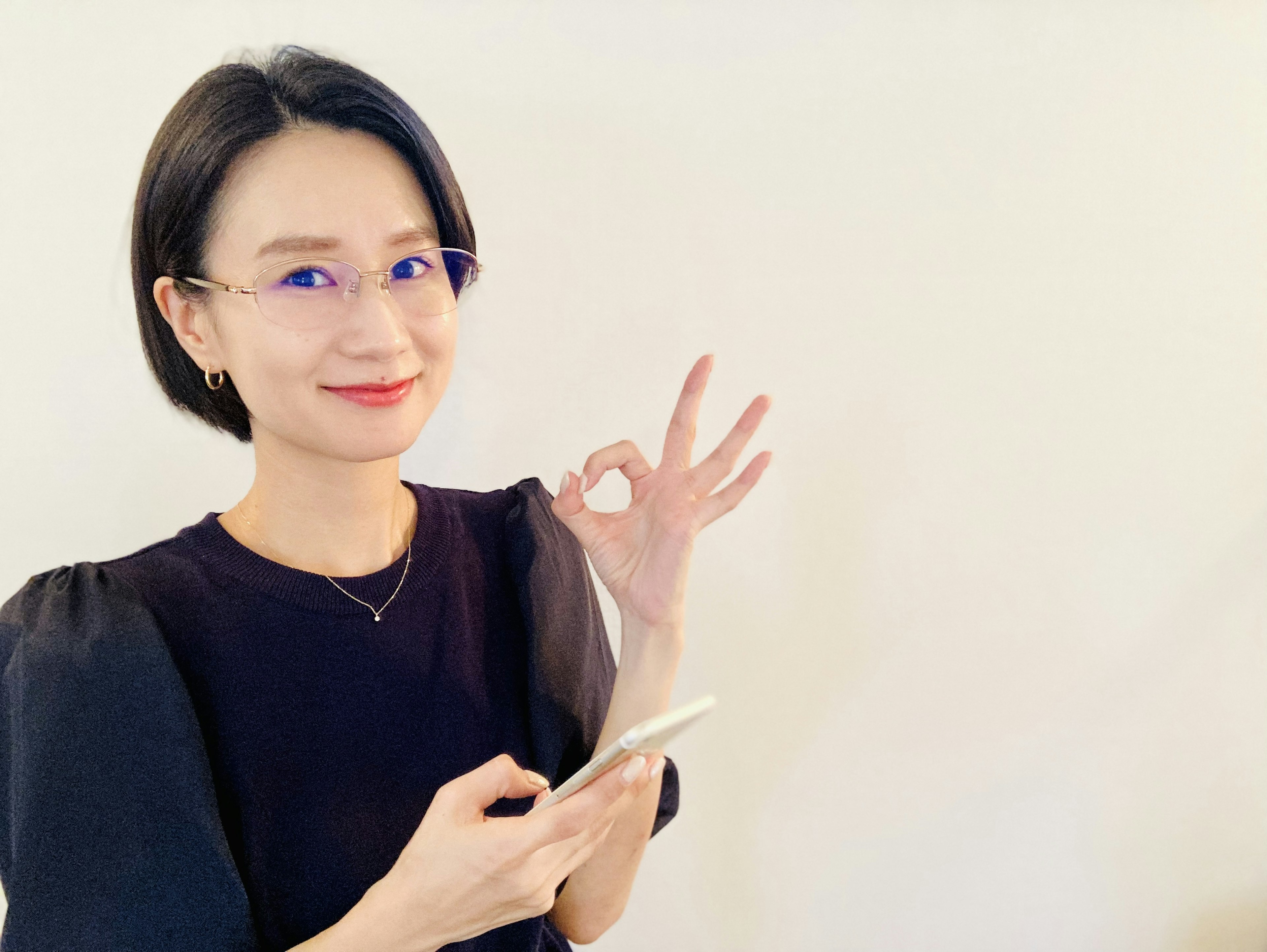 Woman with black hair holding a smartphone and making an OK sign with her fingers in front of a white background