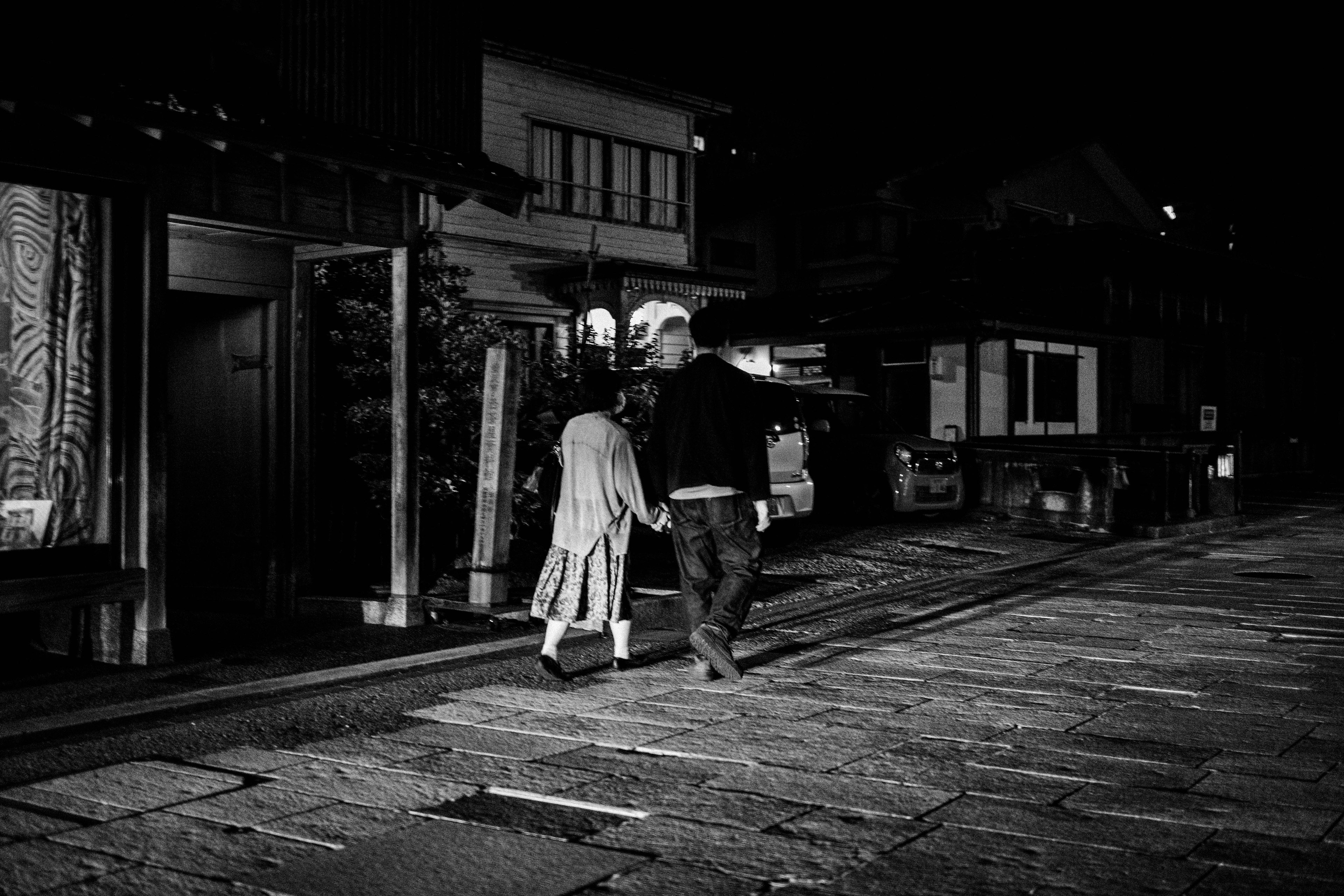 Silhouette of a man and woman walking hand in hand in a nighttime street