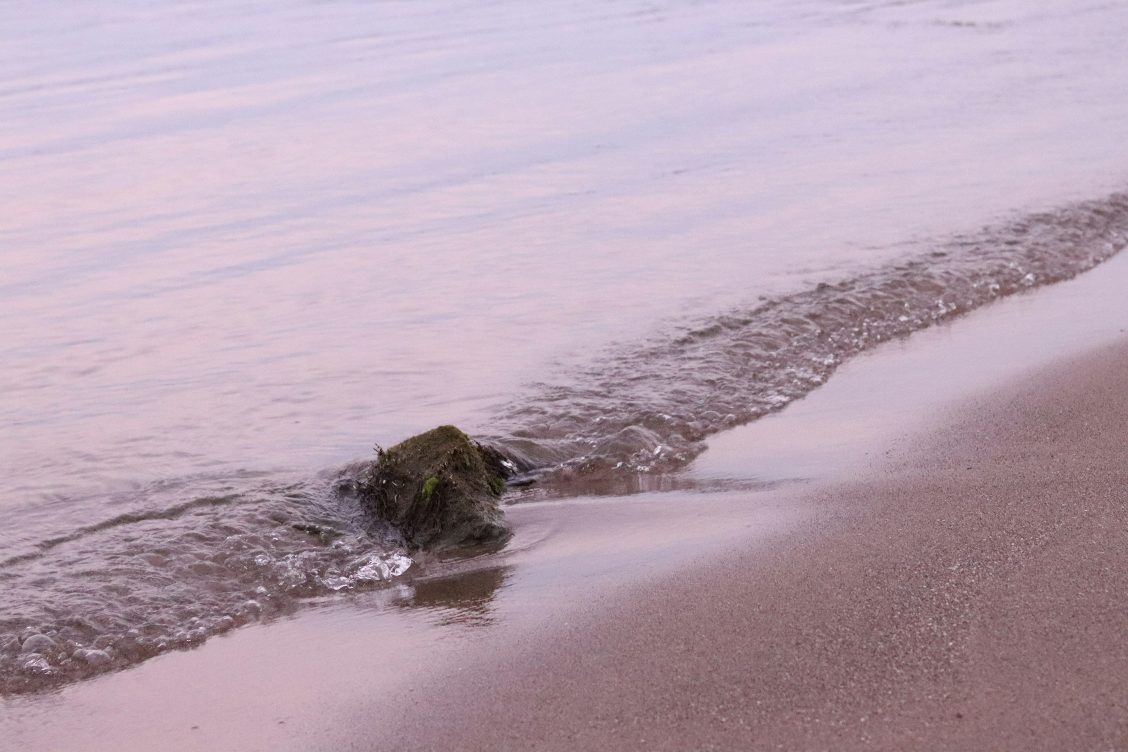 Una pequeña roca parcialmente sumergida en suaves olas en una playa serena