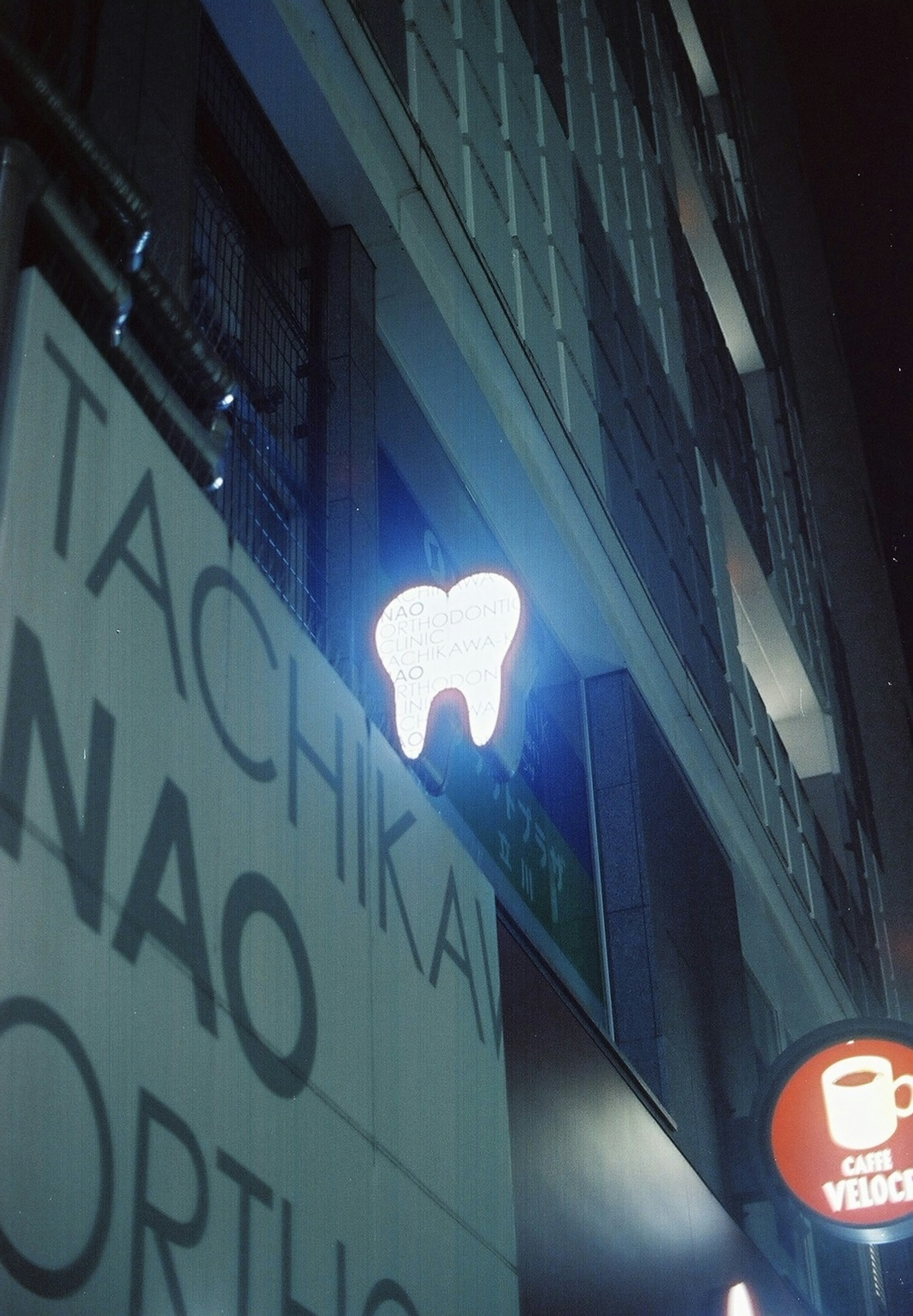 夜の街で光る歯のネオン看板とTachikawa Nao Orthodonticsの看板