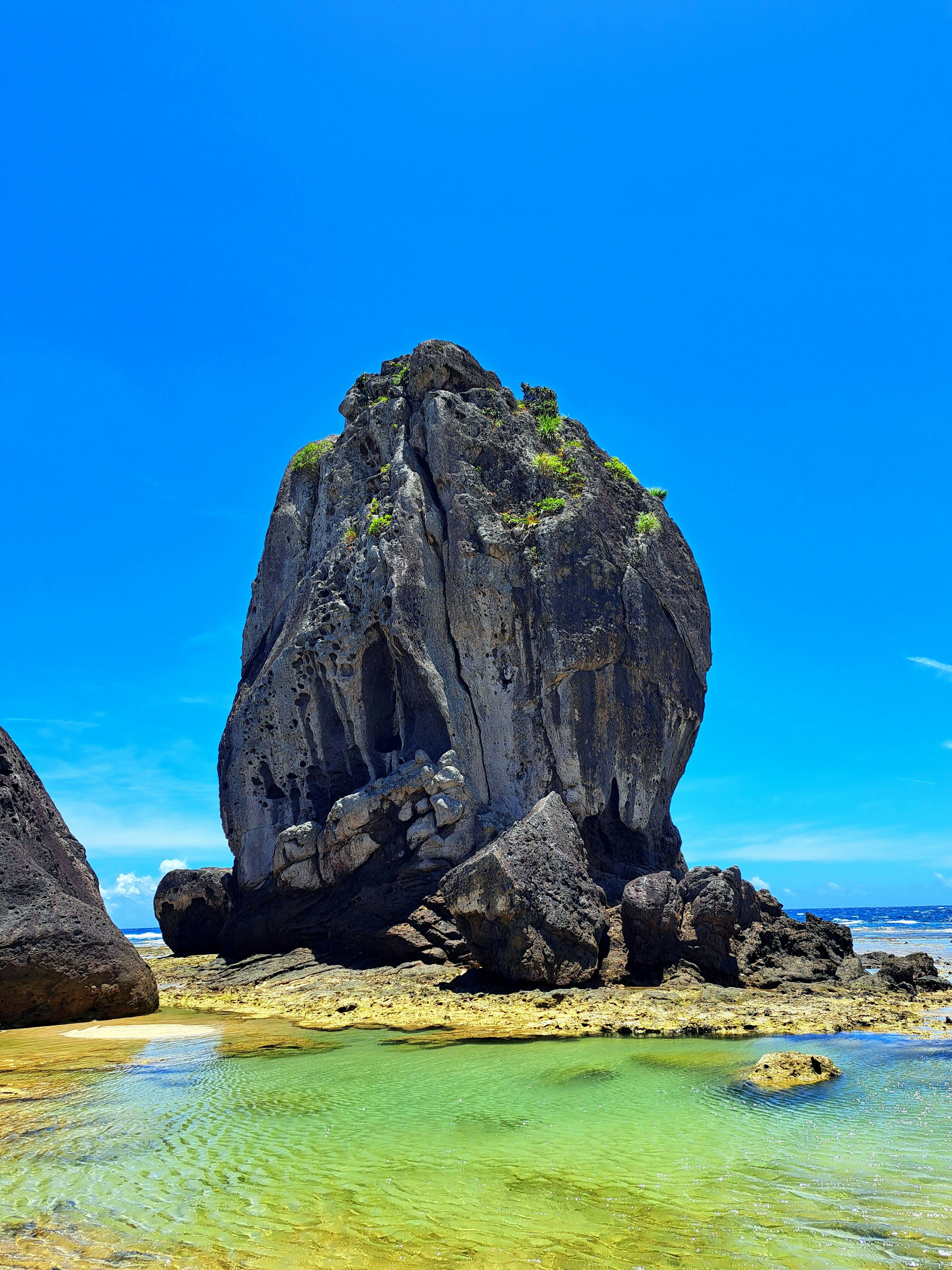 Large rock formation under a clear blue sky with turquoise water