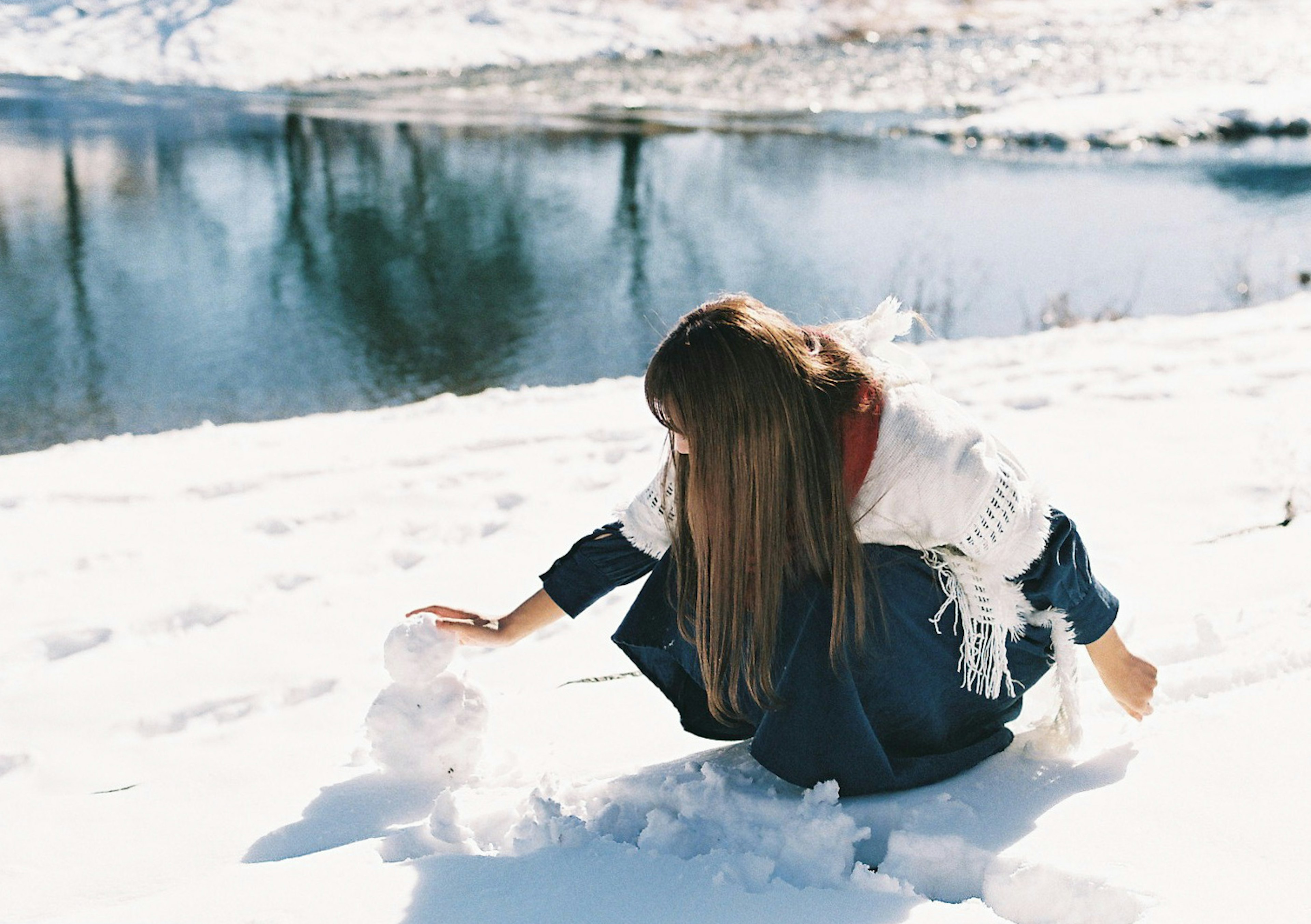 Mujer construyendo un muñeco de nieve en la nieve cerca de un río