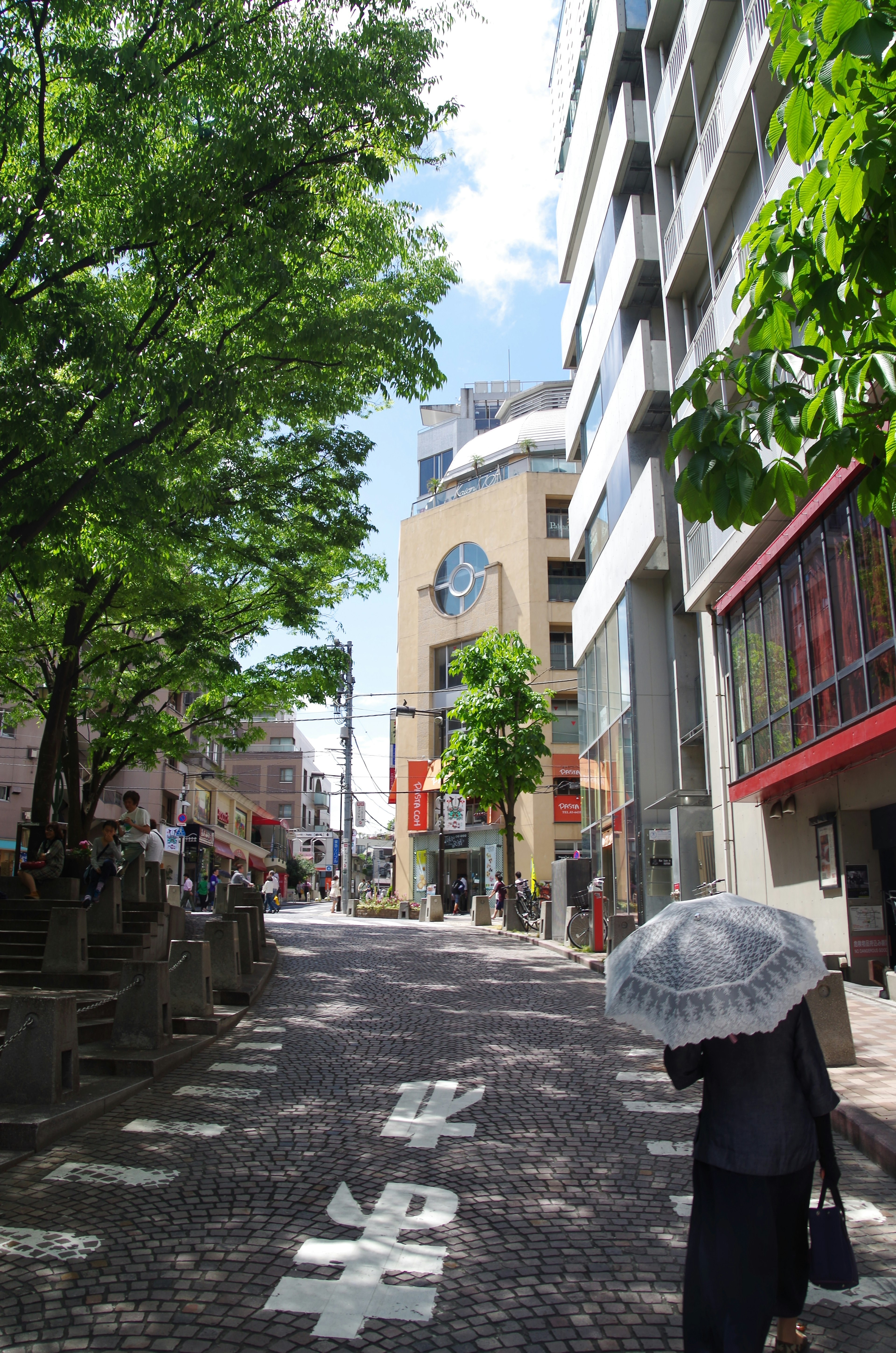 緑の木々に囲まれた静かな通りに傘をさす人がいる