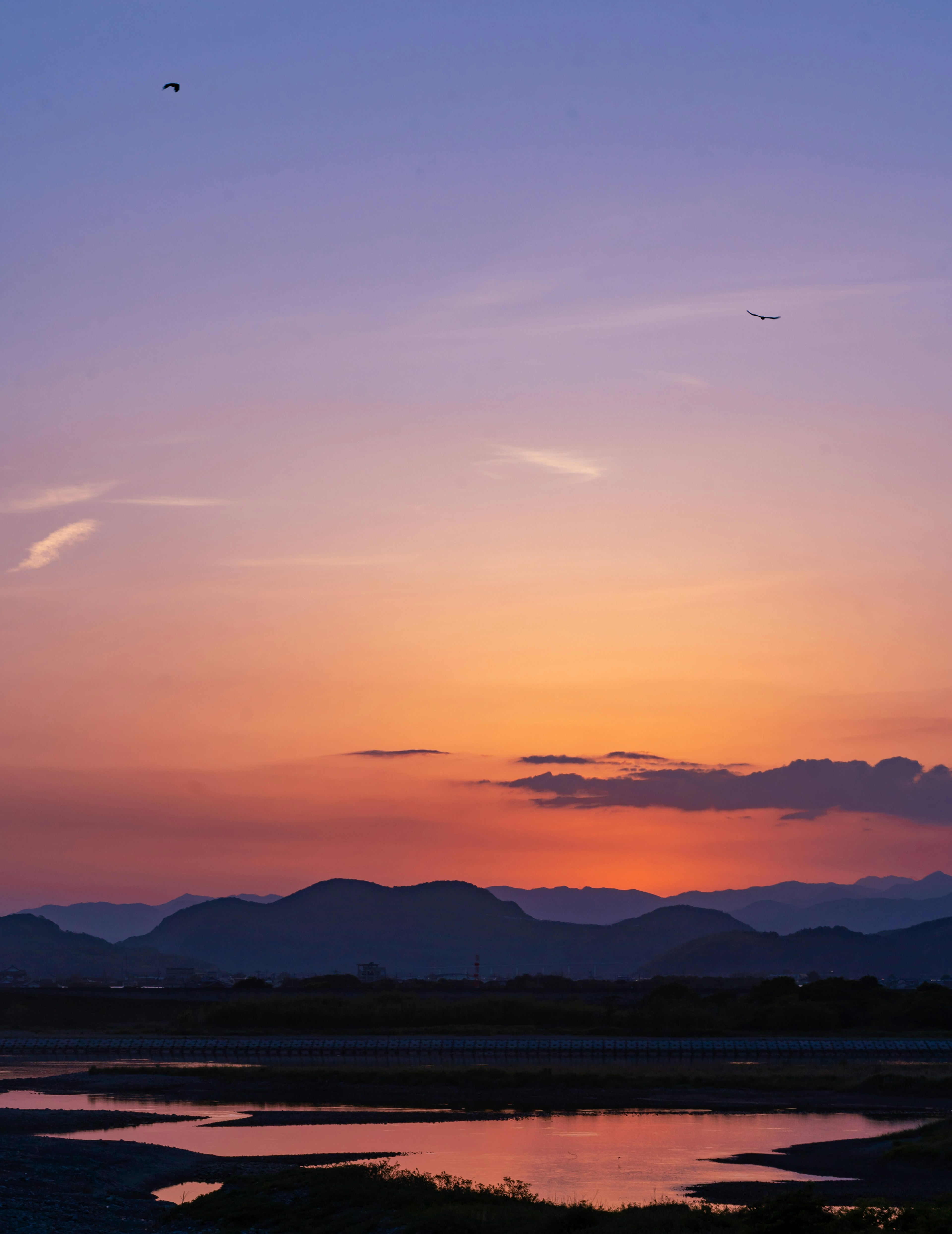 Schöner Sonnenuntergang mit Silhouetten von Bergen und reflektierendem Wasser