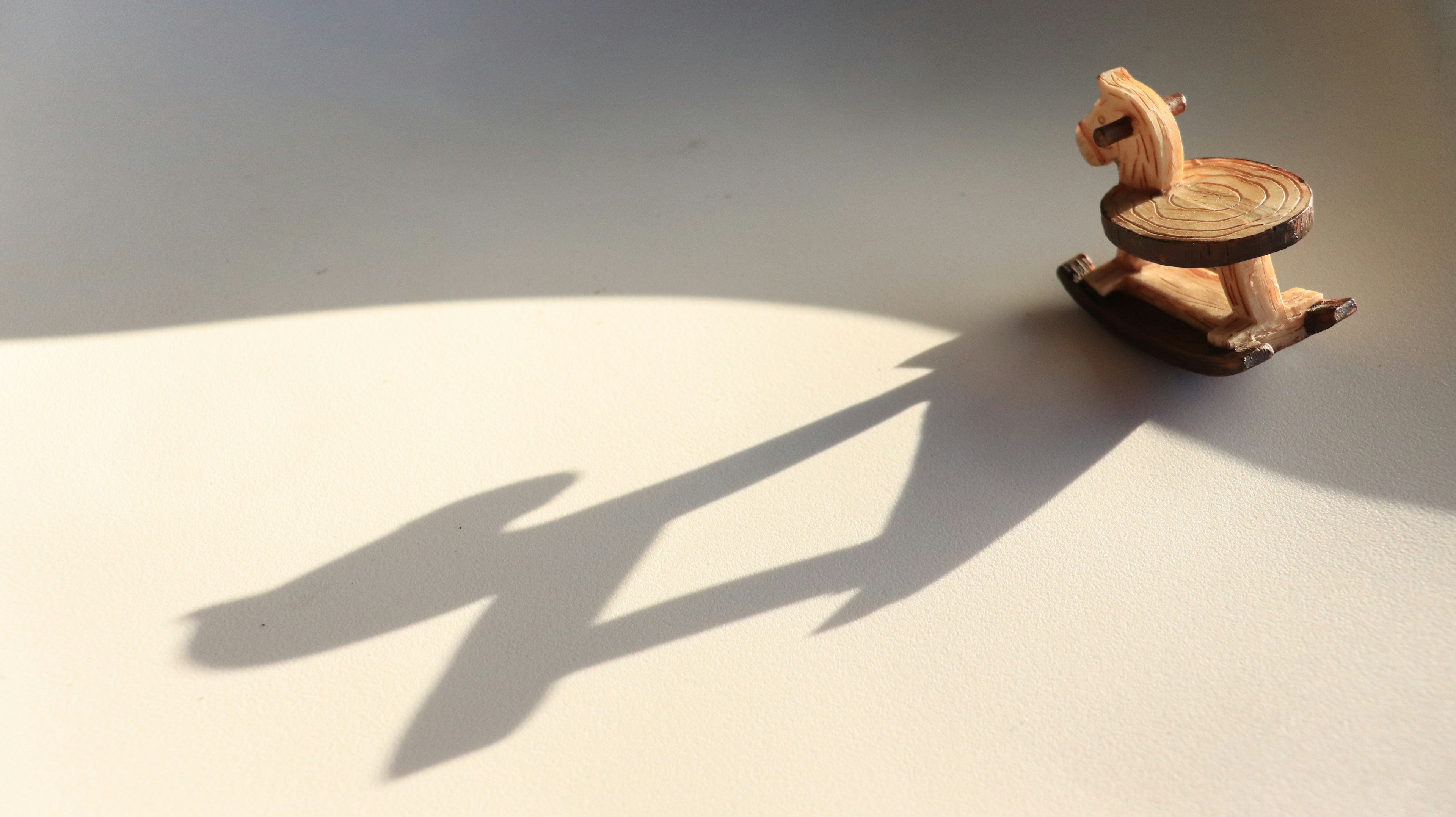 Wooden rocking horse casting a shadow on a light surface