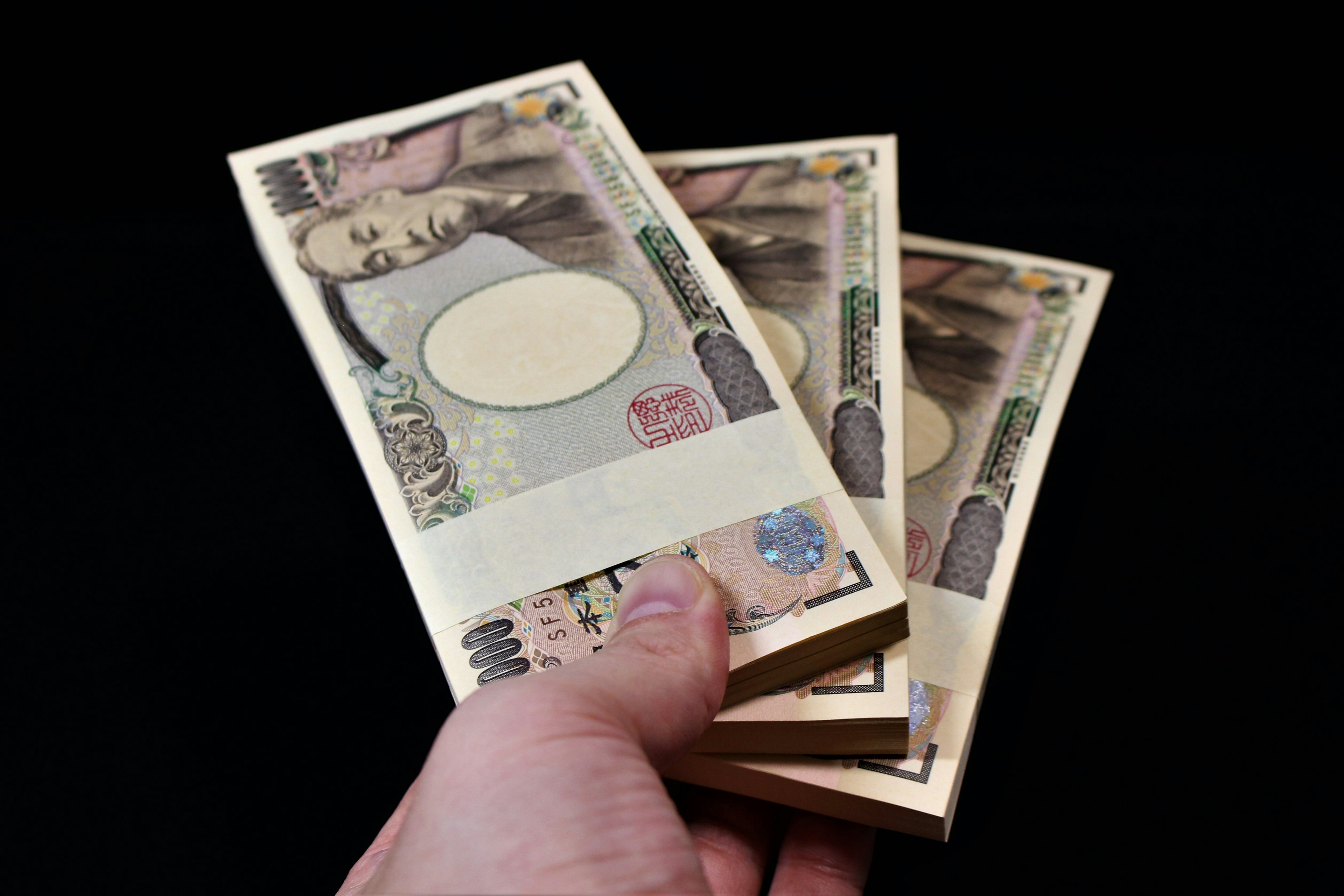 Un paquet de billets de yen japonais tenu dans une main sur un fond noir