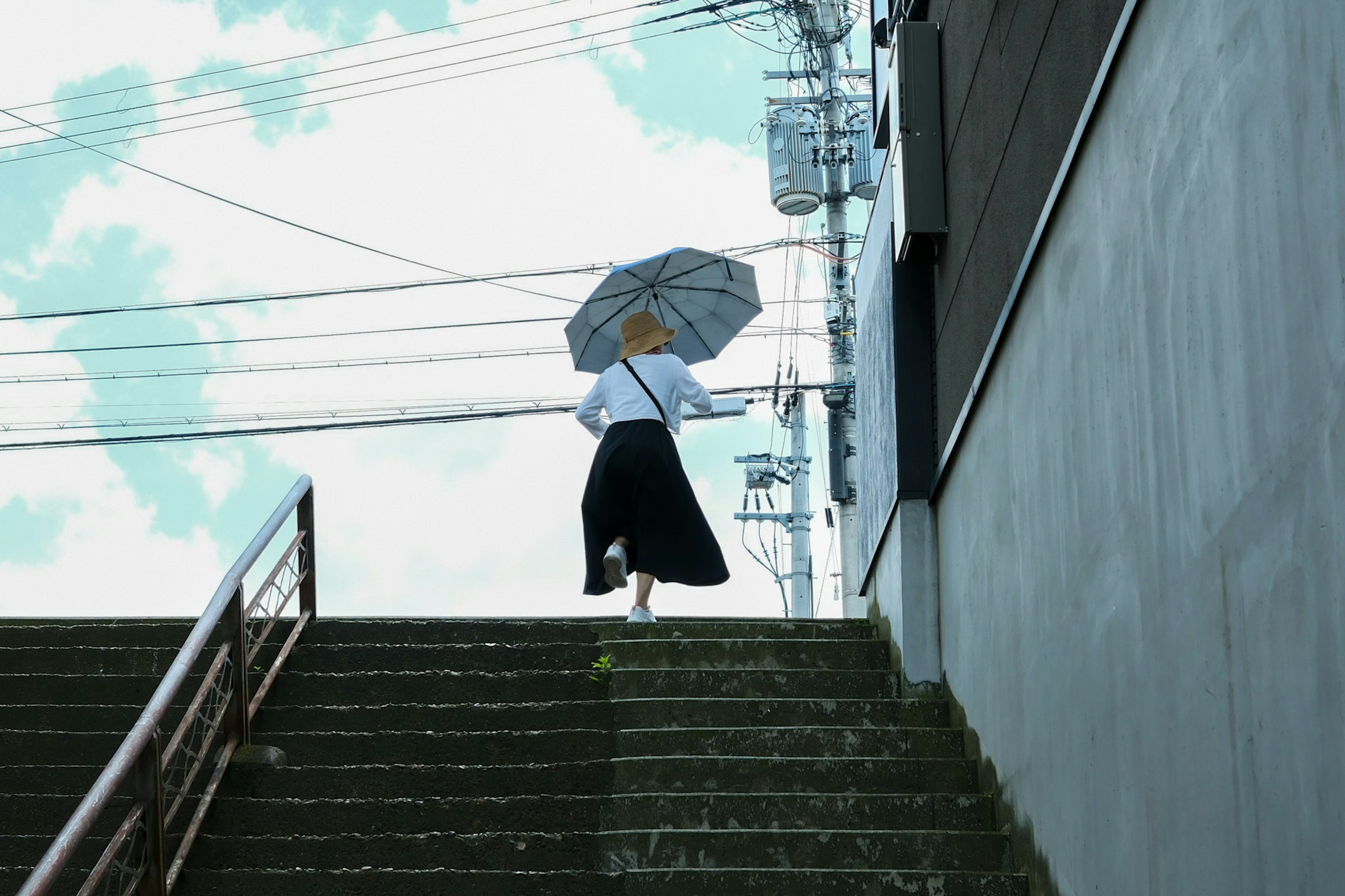 Silhouette of a person holding an umbrella ascending stairs under a blue sky