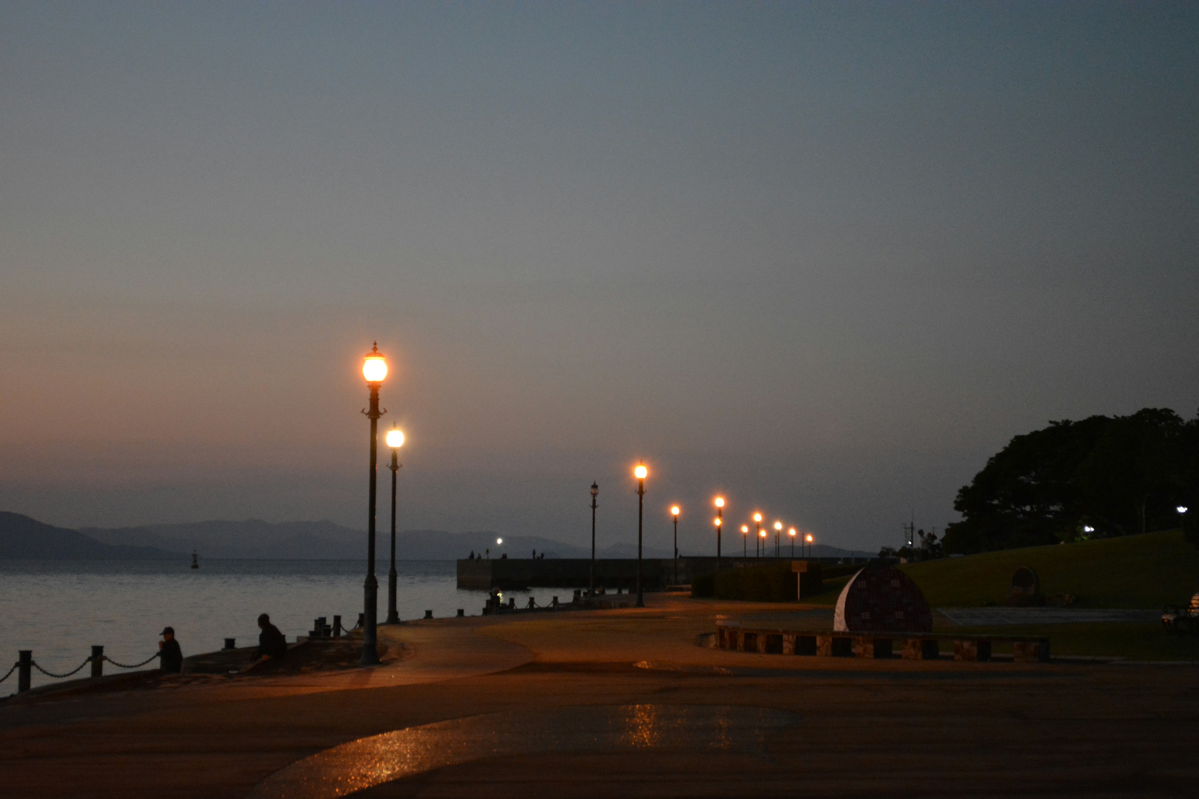 Quiet seaside promenade at dusk with streetlights and people