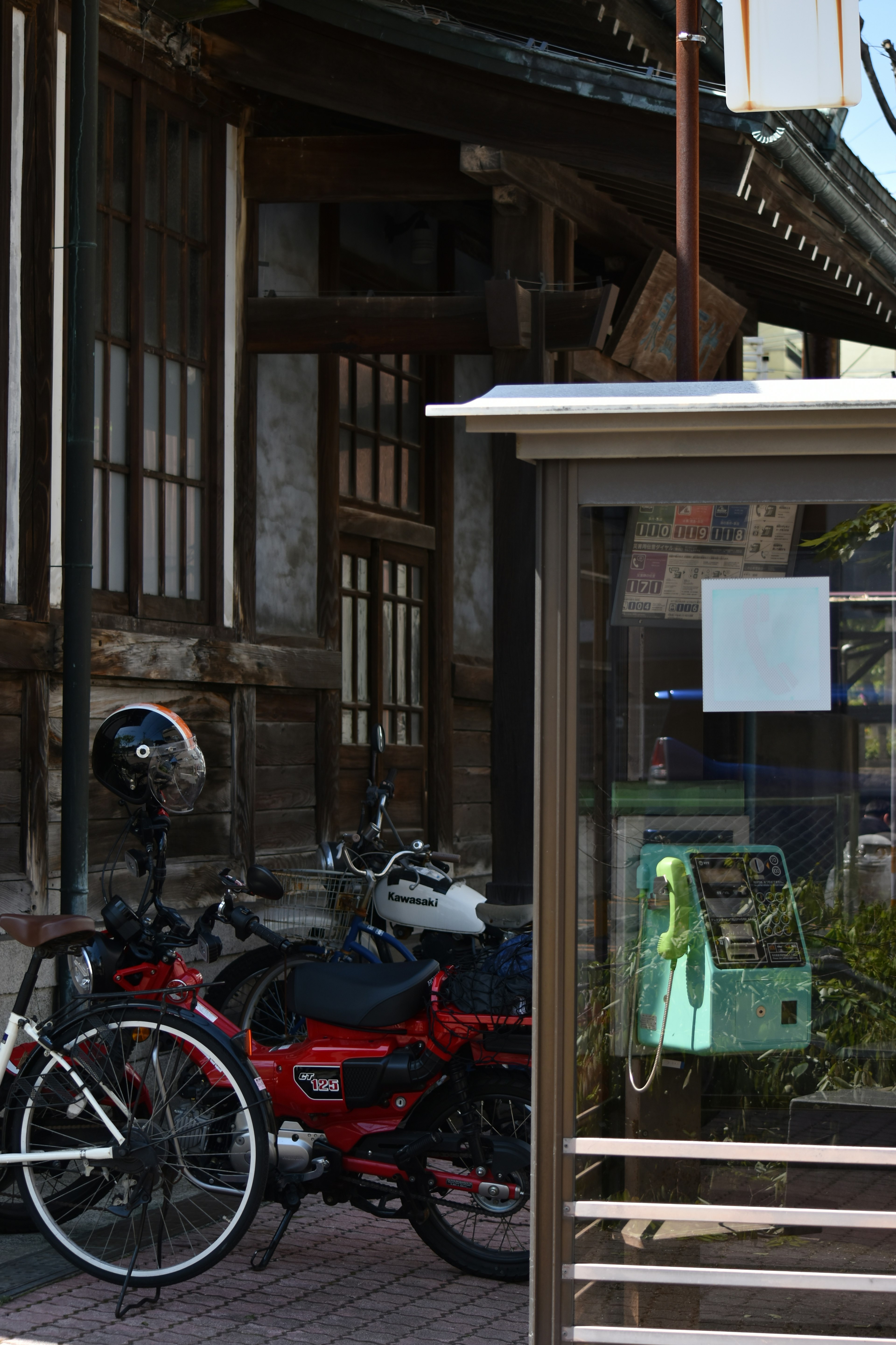 古い日本の建物の前に停められた自転車と公衆電話ボックス