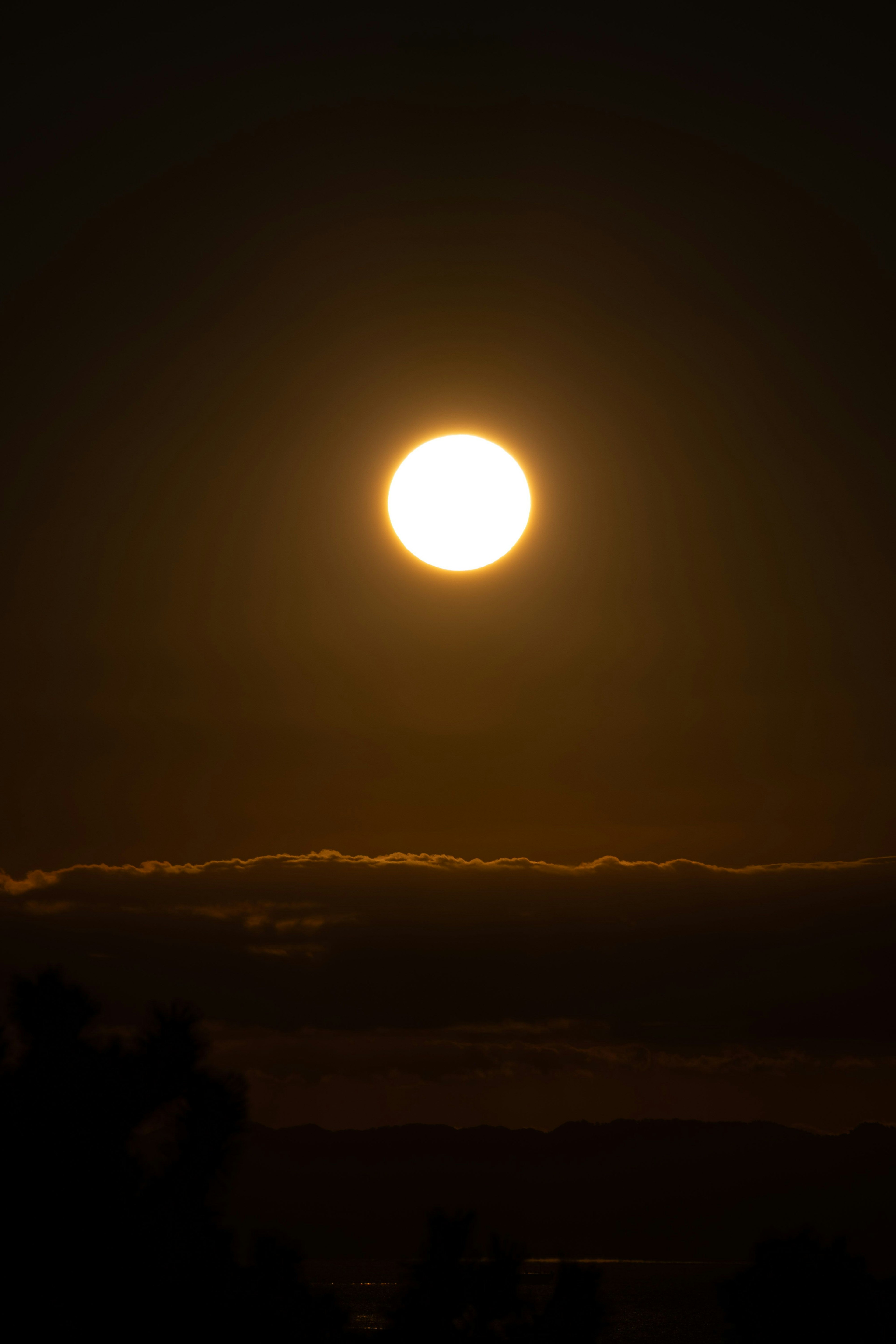 夕暮れ時の太陽が雲の上に輝くシルエット