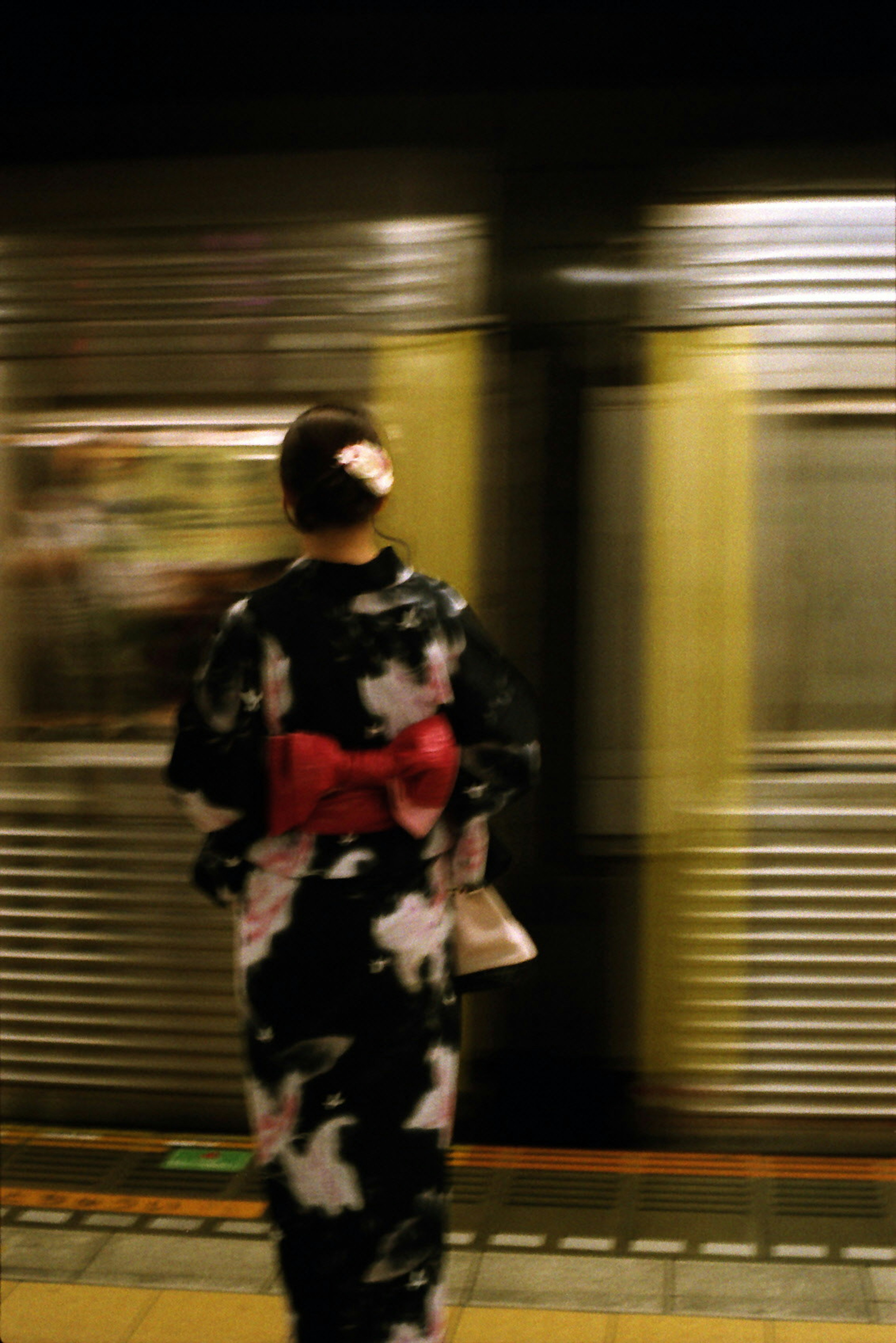 Una donna in kimono in piedi vicino a un treno della metropolitana