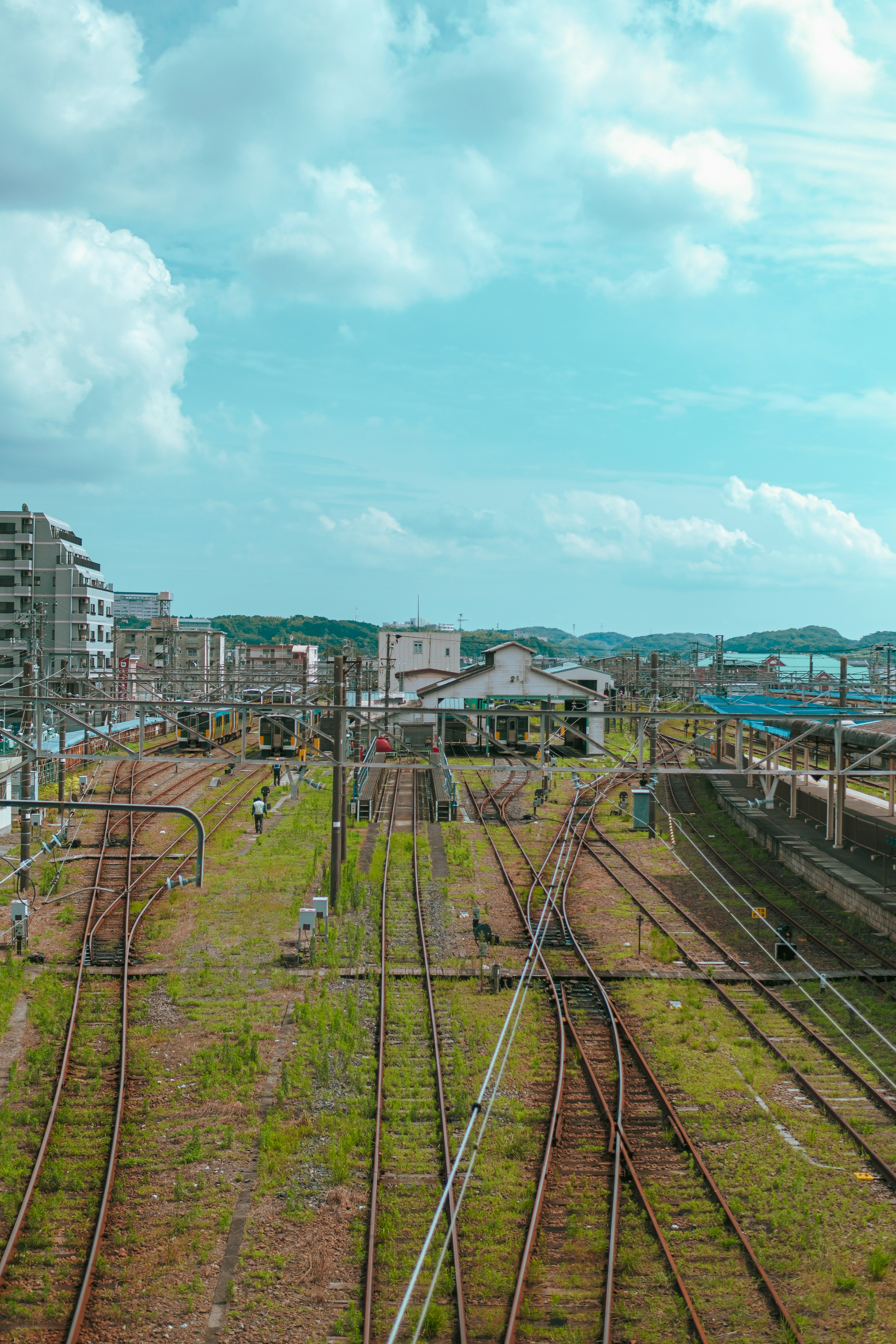 Pemandangan jalur kereta dan stasiun dengan rumput hijau dan langit biru