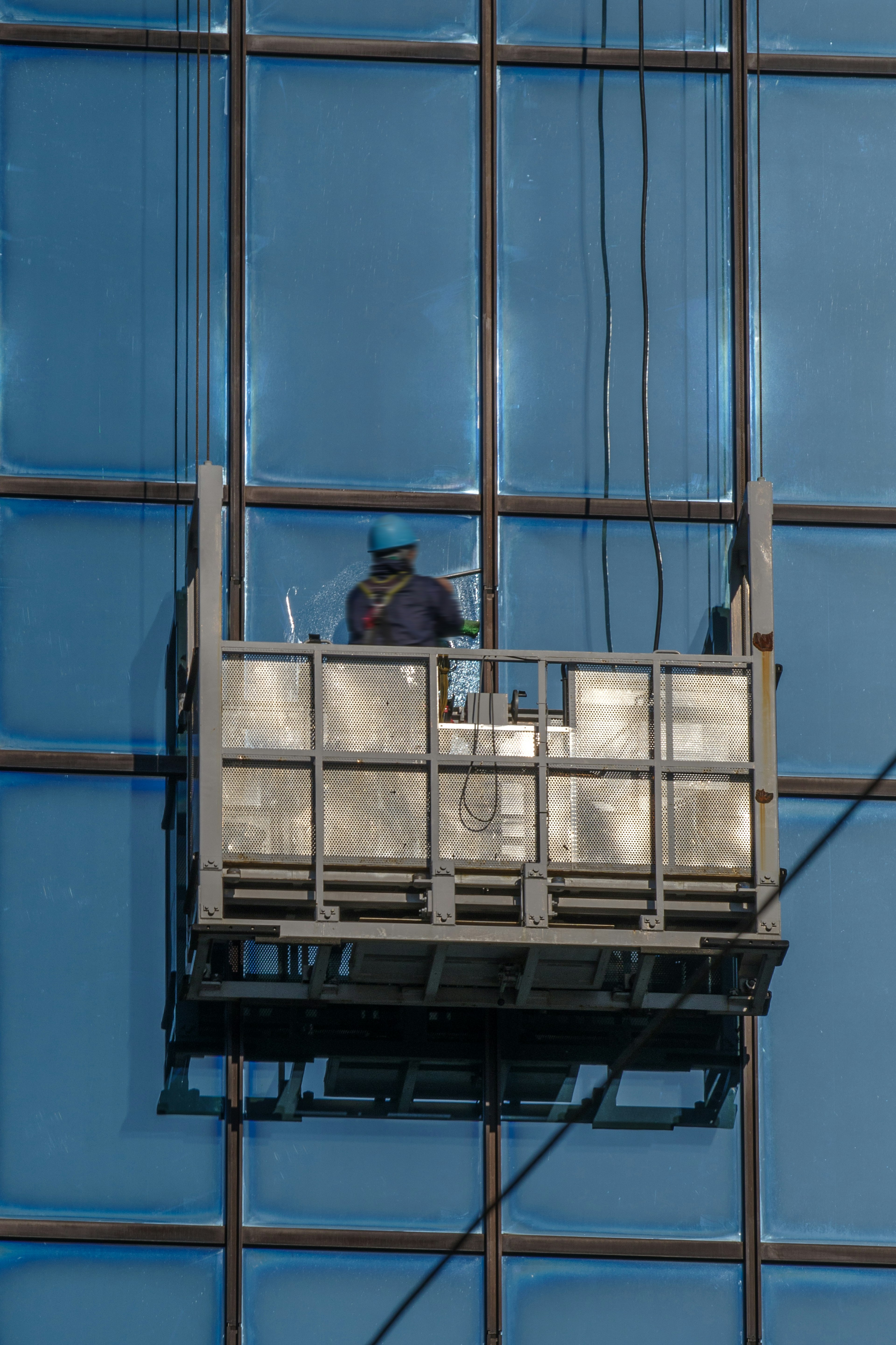 Pekerja di platform tergantung membersihkan gedung kaca biru